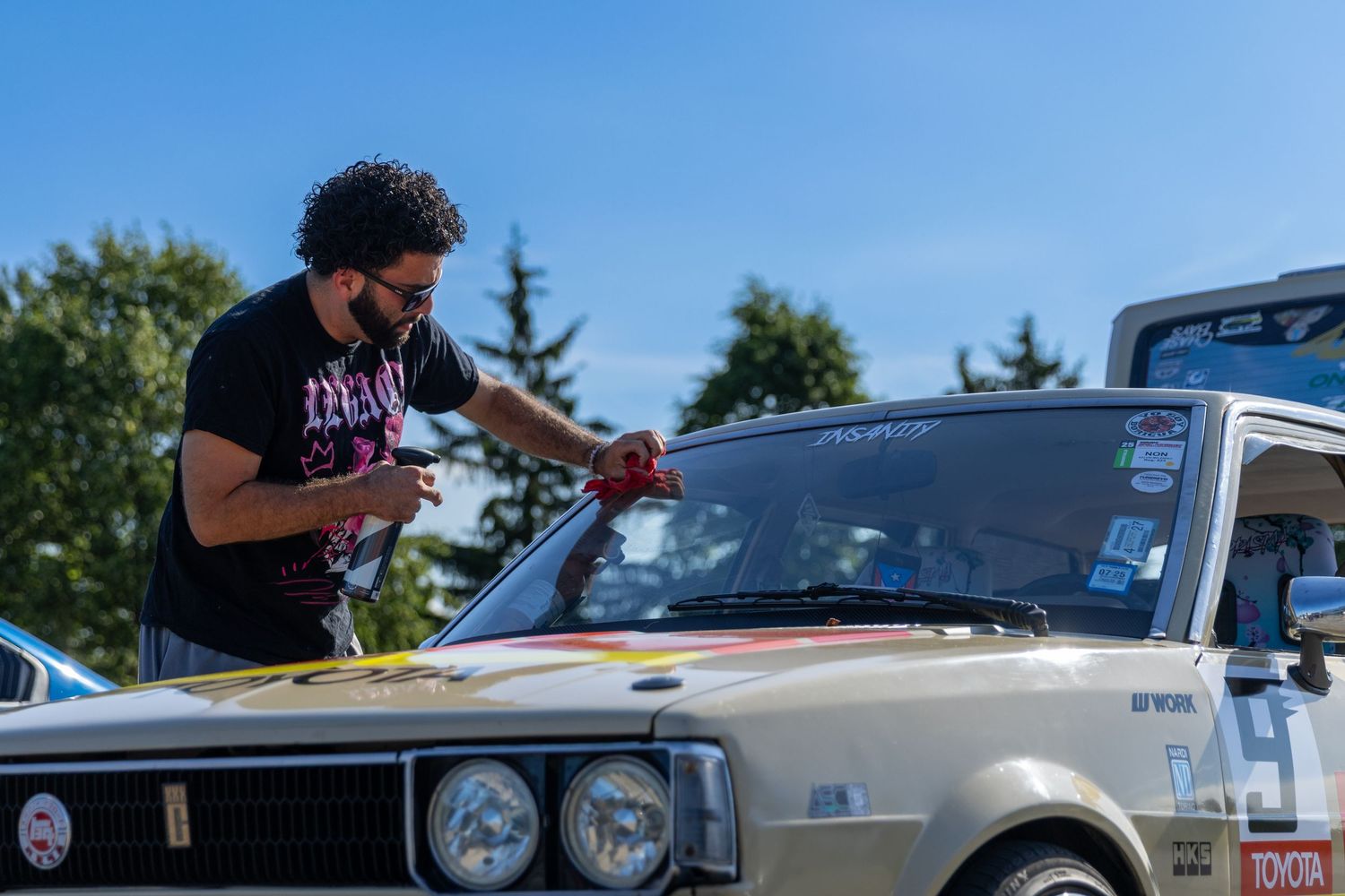 Person cleaning the windshield of a classic car on a sunny day.