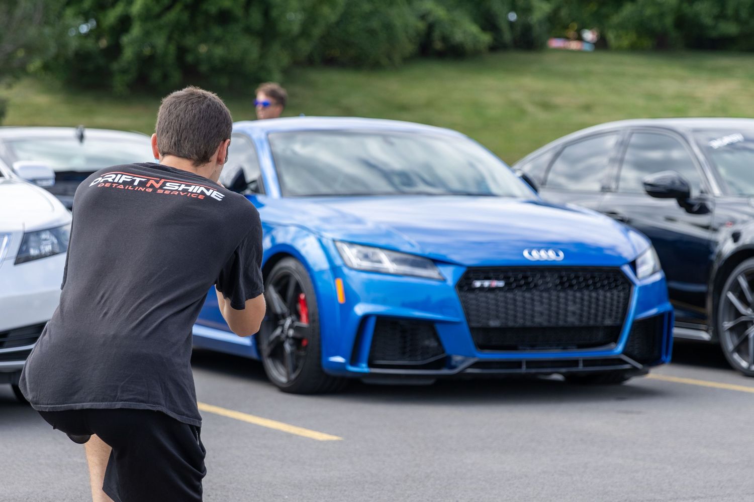 People gather at a luxury car meetup displaying exotic cars including a blue Lamborghini and other sports vehicles.