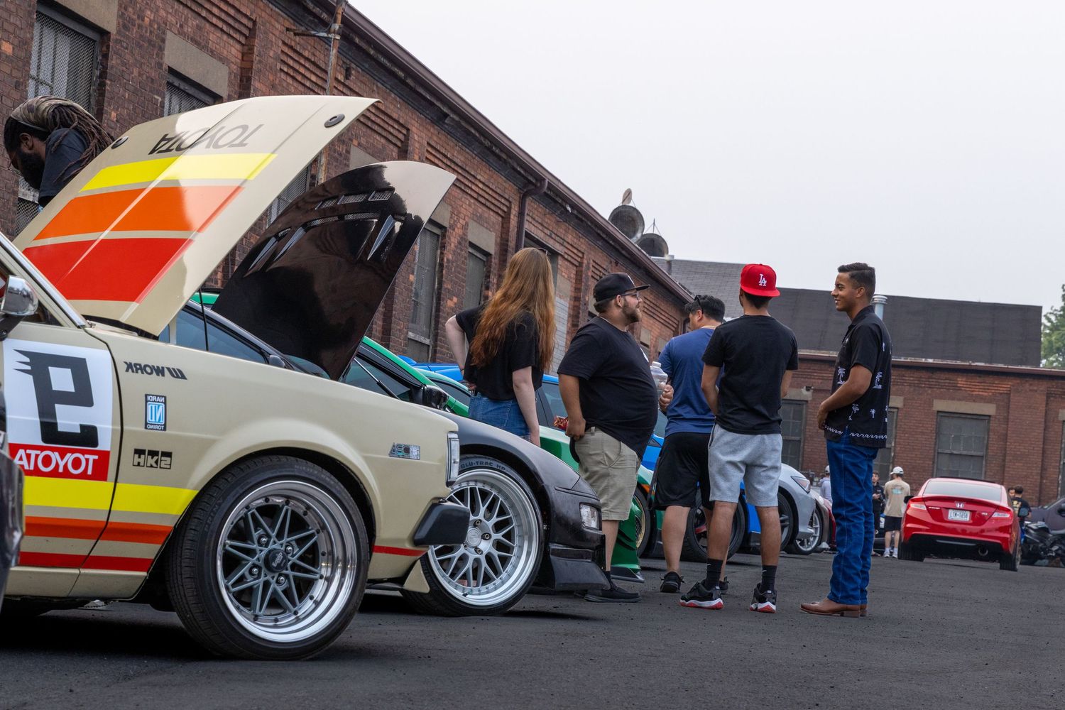 A row of modified cars with custom rims and suspensions lined up at a car meet event on a paved lot.