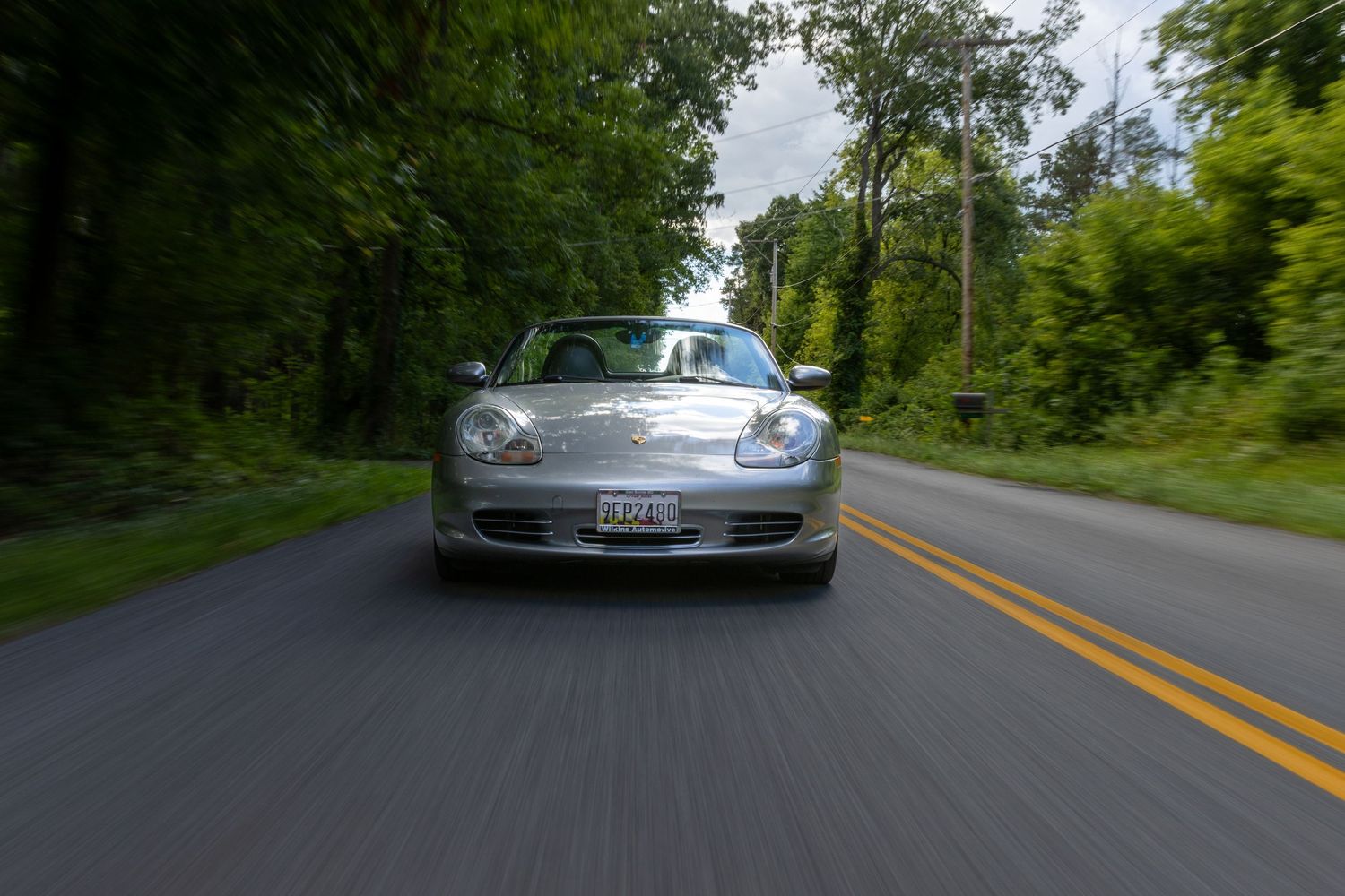 Silver Mercedes-Benz SLR McLaren supercar driving on a winding forest road during daytime.