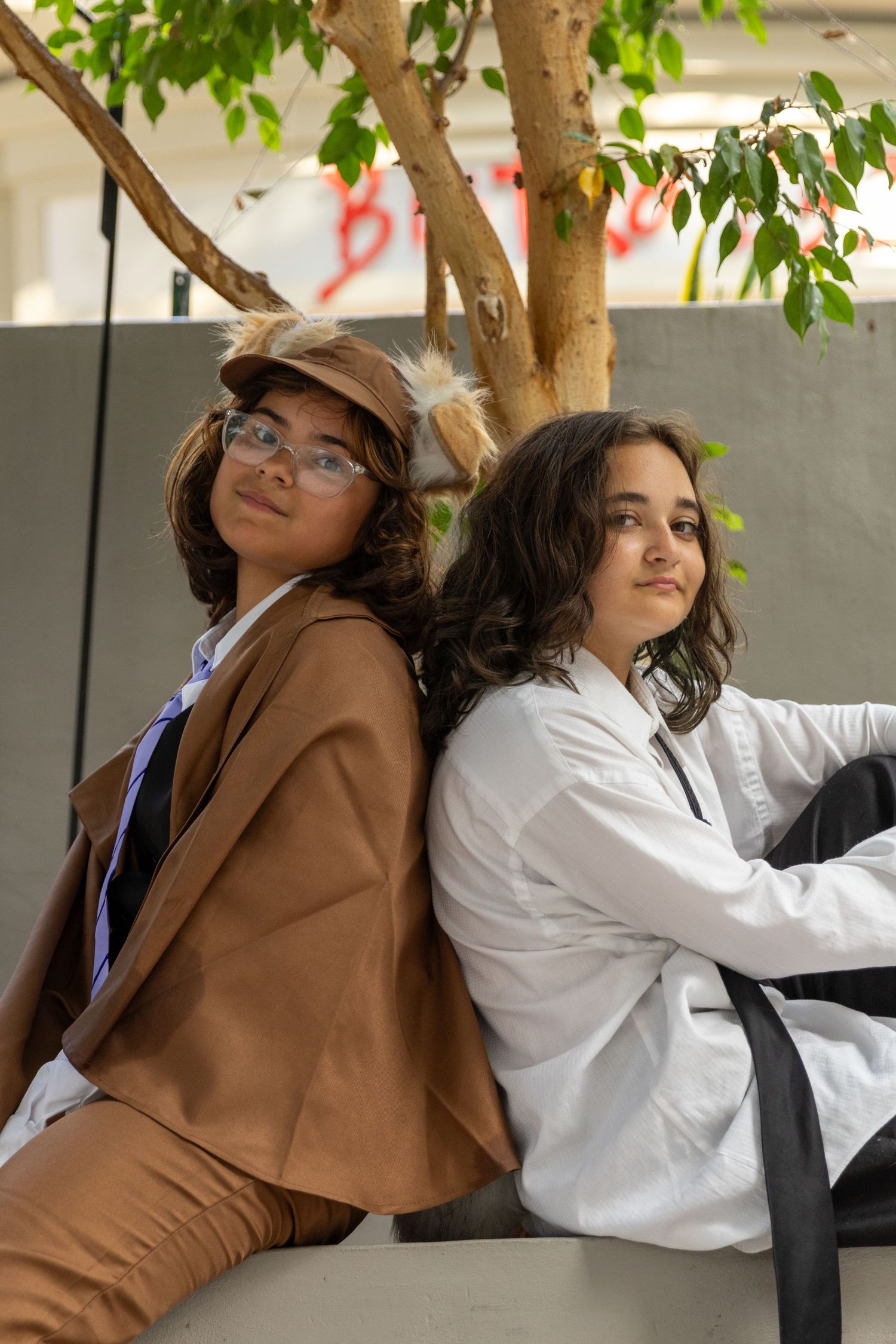 People wearing white coats and brown jackets pose dramatically against a tree with green leaves in a series of photos.