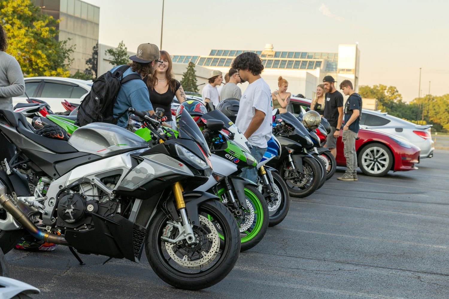 Multiple sport bikes lined up in a parking lot during a motorcycle meetup at dusk.