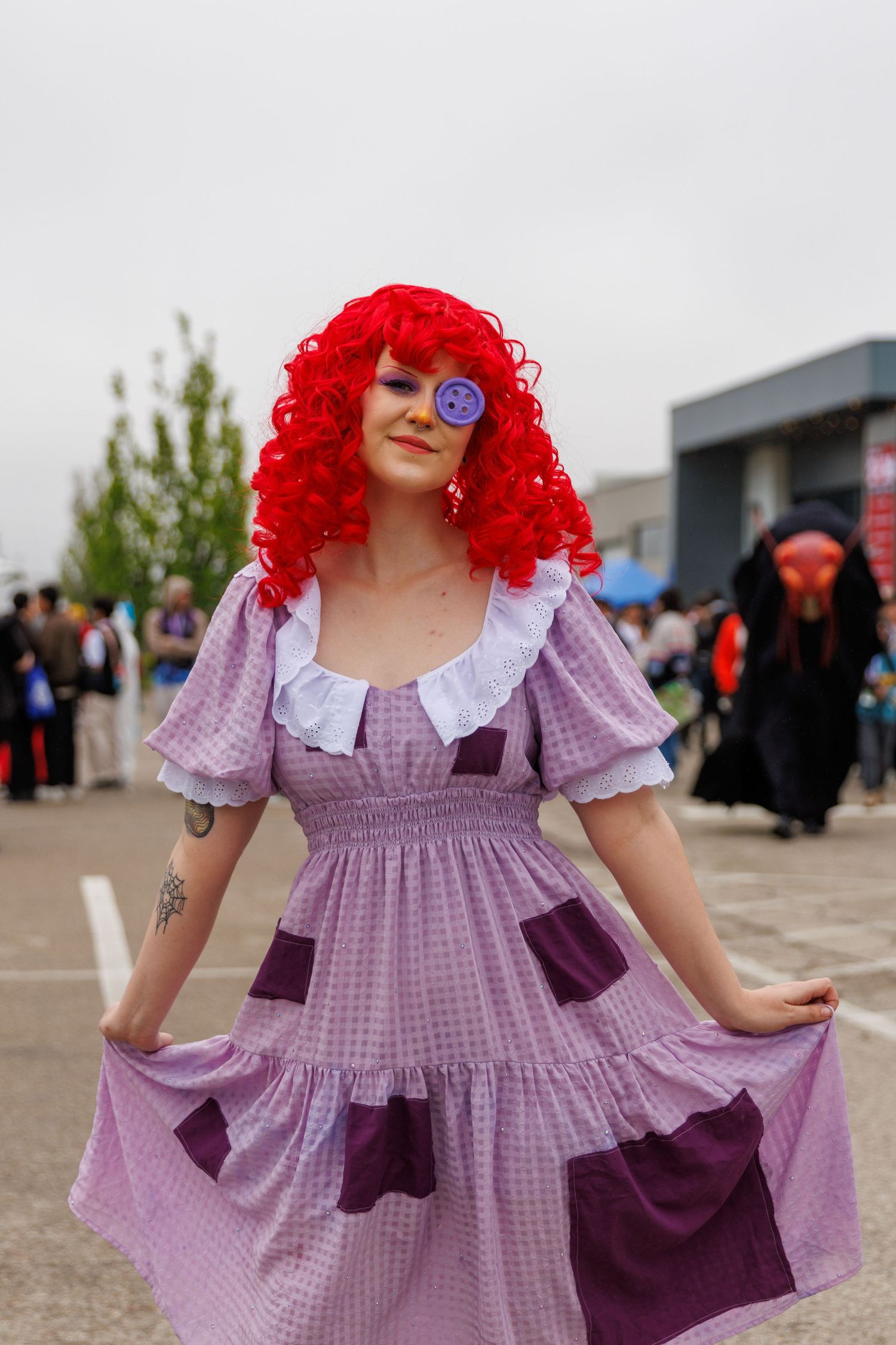 Woman in purple gingham dress and red curly wig cosplaying as a rag doll at an outdoor convention.