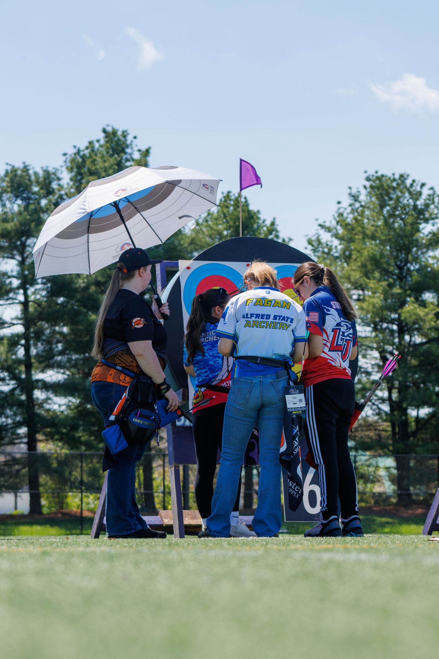 Group of female archers score targets at outdoor archery competition on sunny day.