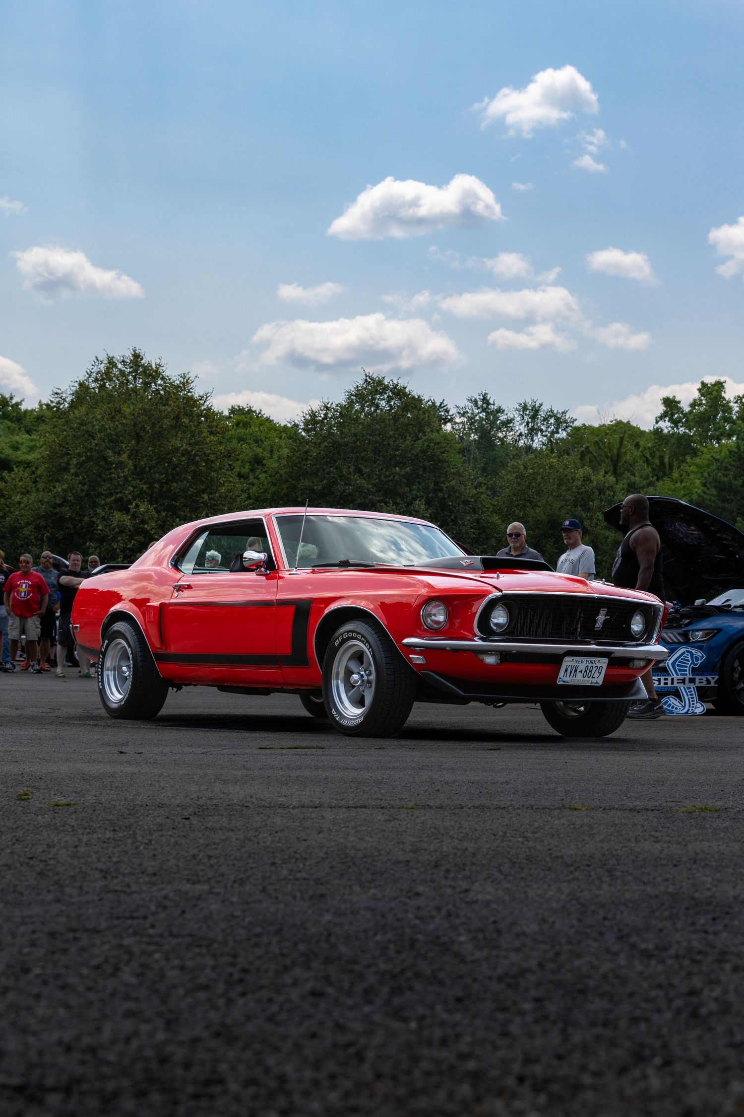 Two classic red Ford Mustangs displayed side by side at an outdoor car show against a blue summer sky.