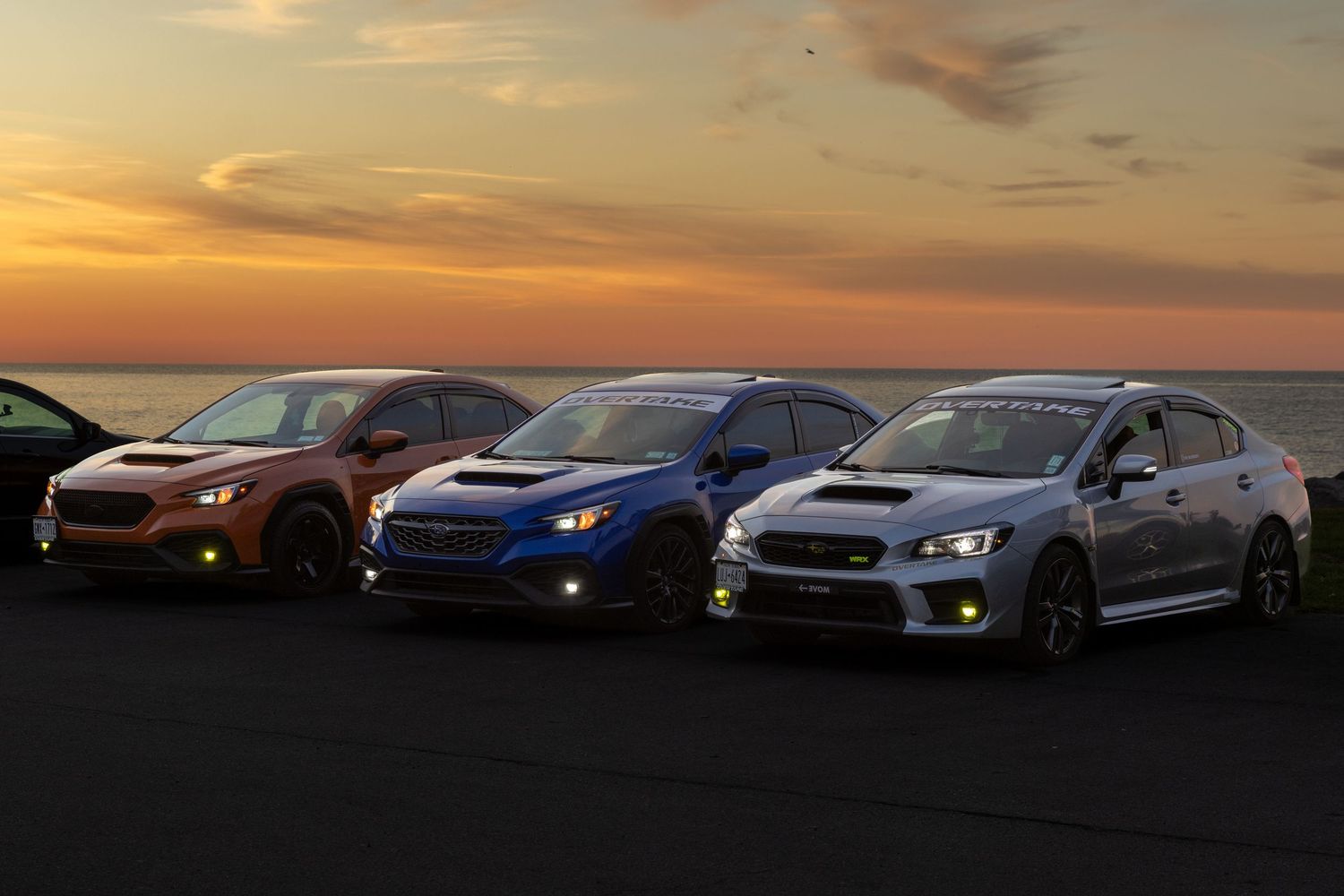 A row of Subaru WRX and STI performance cars parked together against a dramatic sunset sky.