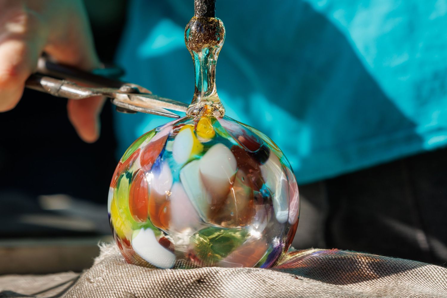 Colorful handmade glass globe pendant being crafted with a torch, showcasing vibrant swirls of red, blue, and green.
