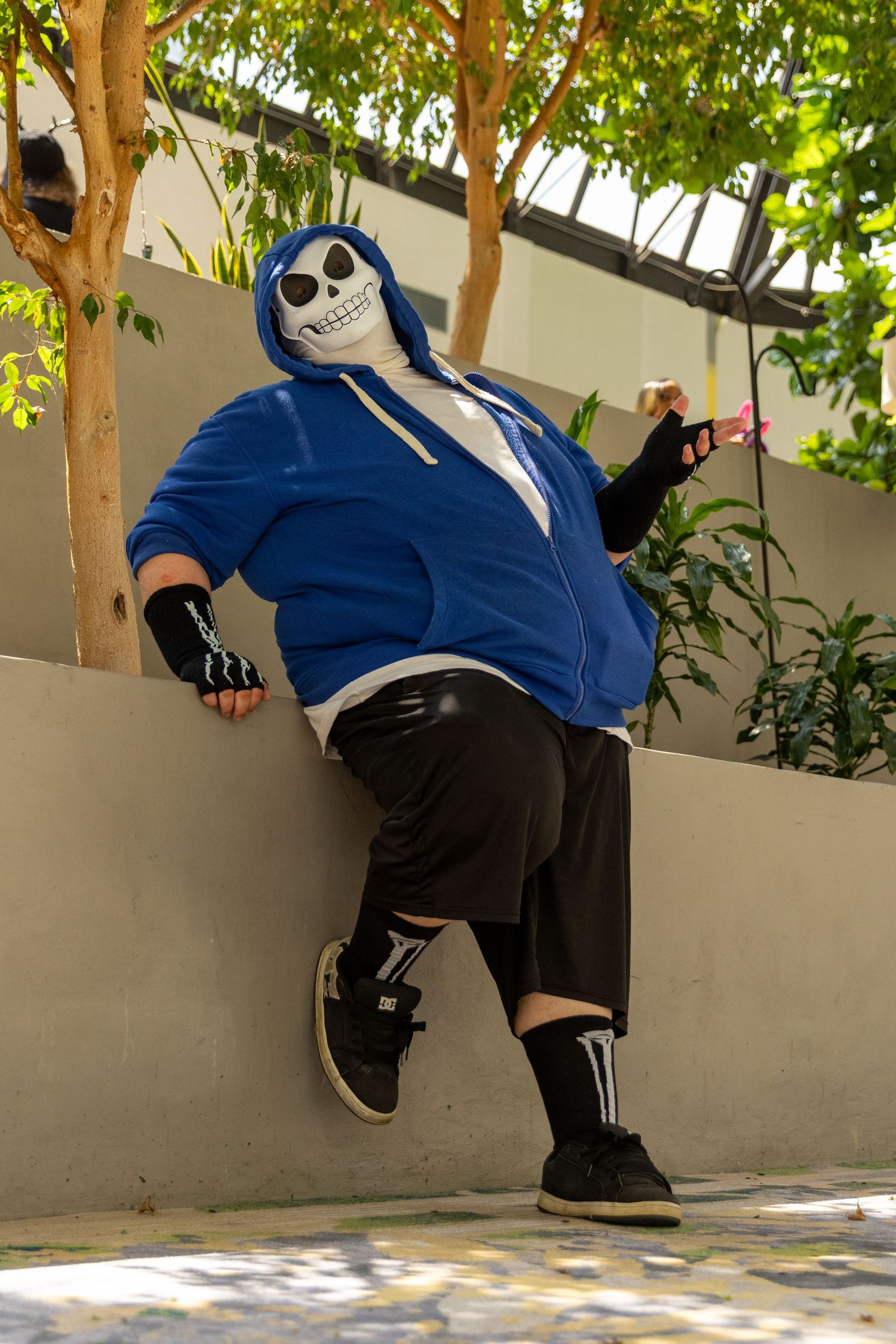 A person performing parkour moves along a wall wearing a blue hoodie, black pants, and ankle length socks.