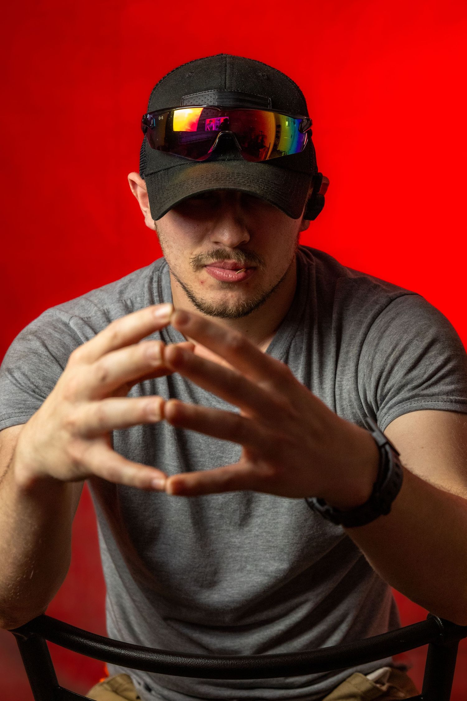Portrait against red background showing hands gesturing with reflective sports sunglasses and cap.