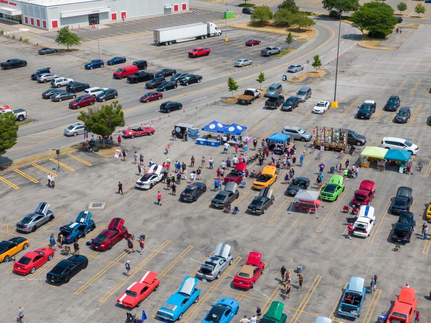 Aerial view of colorful cars parked in rows at a shopping center parking lot on a sunny day.