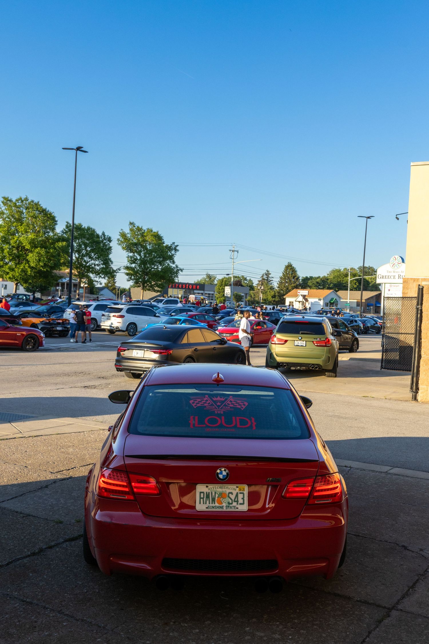Red BMW M3 with custom decals parked in a crowded lot at sunset.