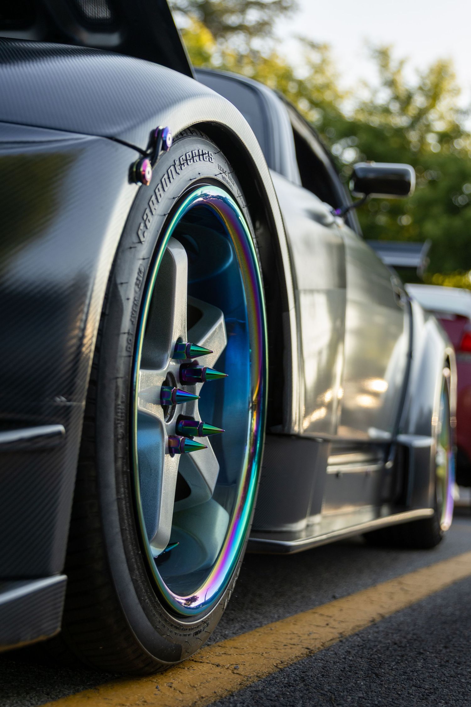 A matte black car with colorful rainbow iridescent rims and wide stance tires photographed at ground level.