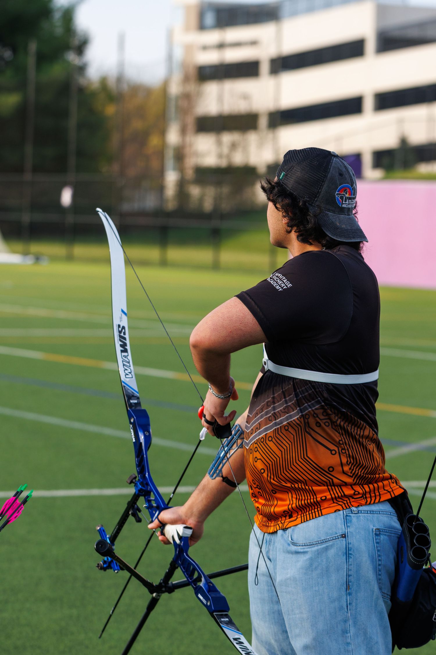Competitive archer aiming a recurve bow on an outdoor field during an archery tournament.