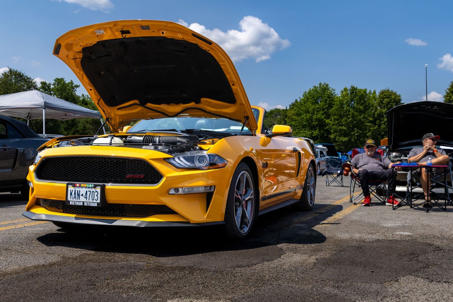 Yellow sports cars with open hoods displayed at a car show in a parking lot.