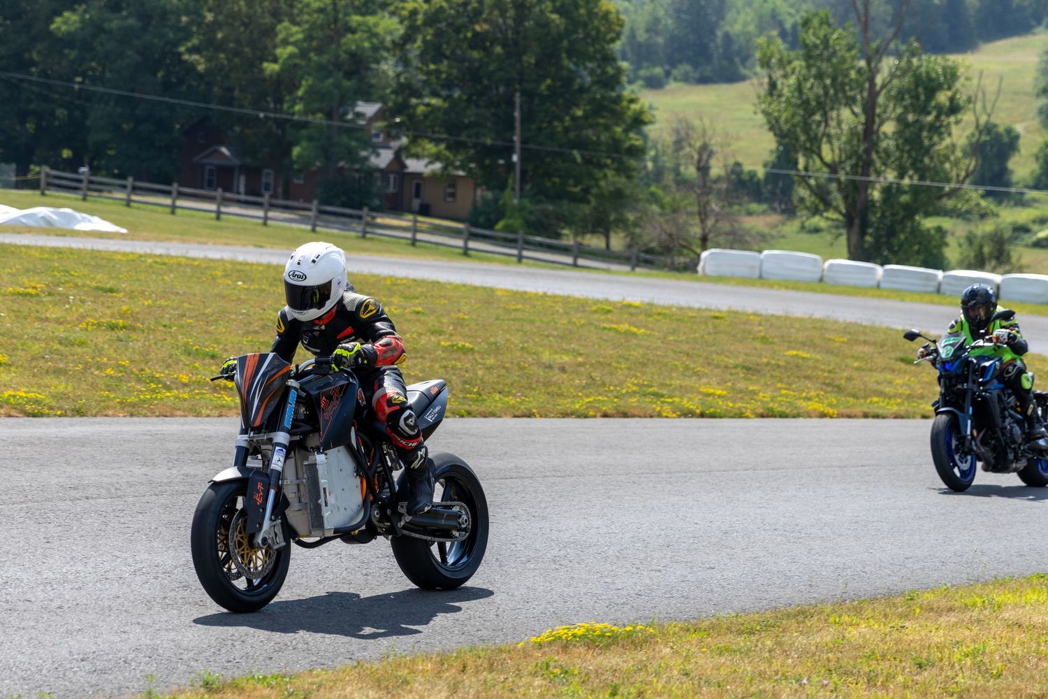 Motorcyclist leans into a curve on a winding mountain road with scenic green hills in the background.