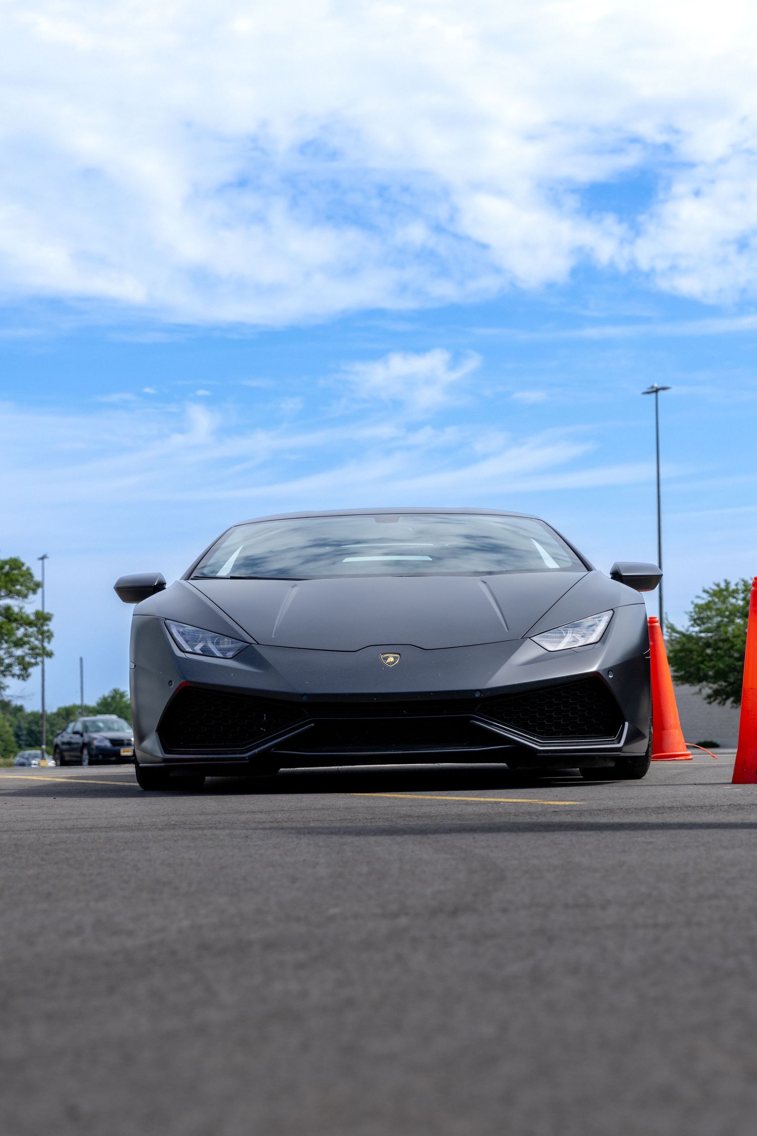 Low angle view of a sleek black Lamborghini sports car against a bright blue sky with wispy clouds.