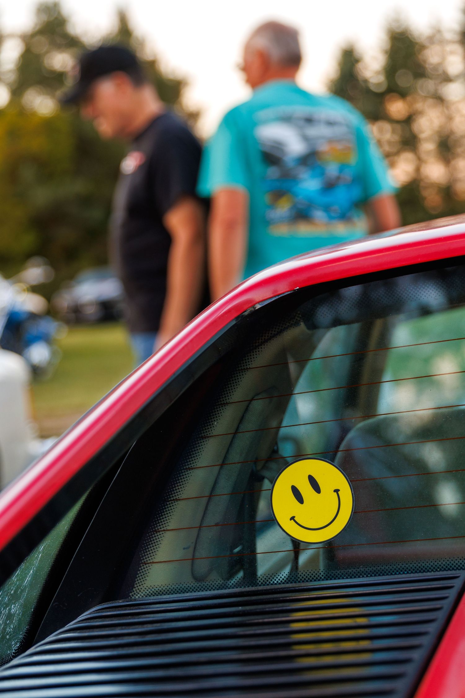A yellow smiley face sticker appears on a red car's rear window in a progressive sequence of photos.