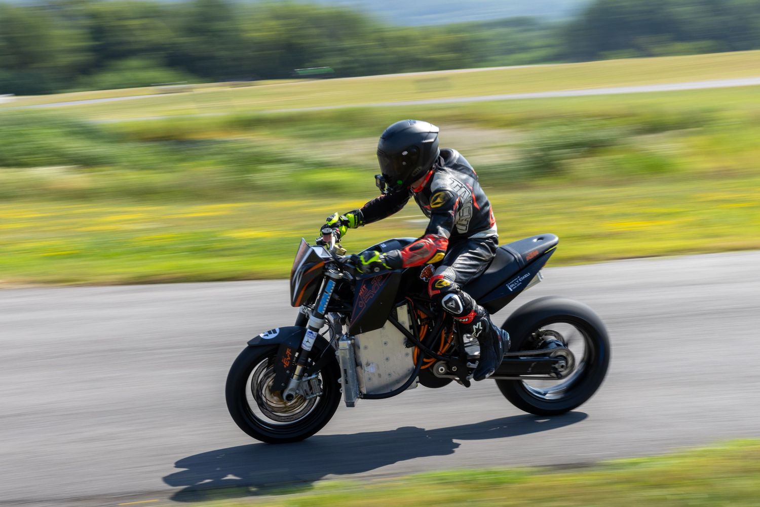 Motorcyclist leans into sharp turn on racetrack while riding orange and black sportbike at high speed.