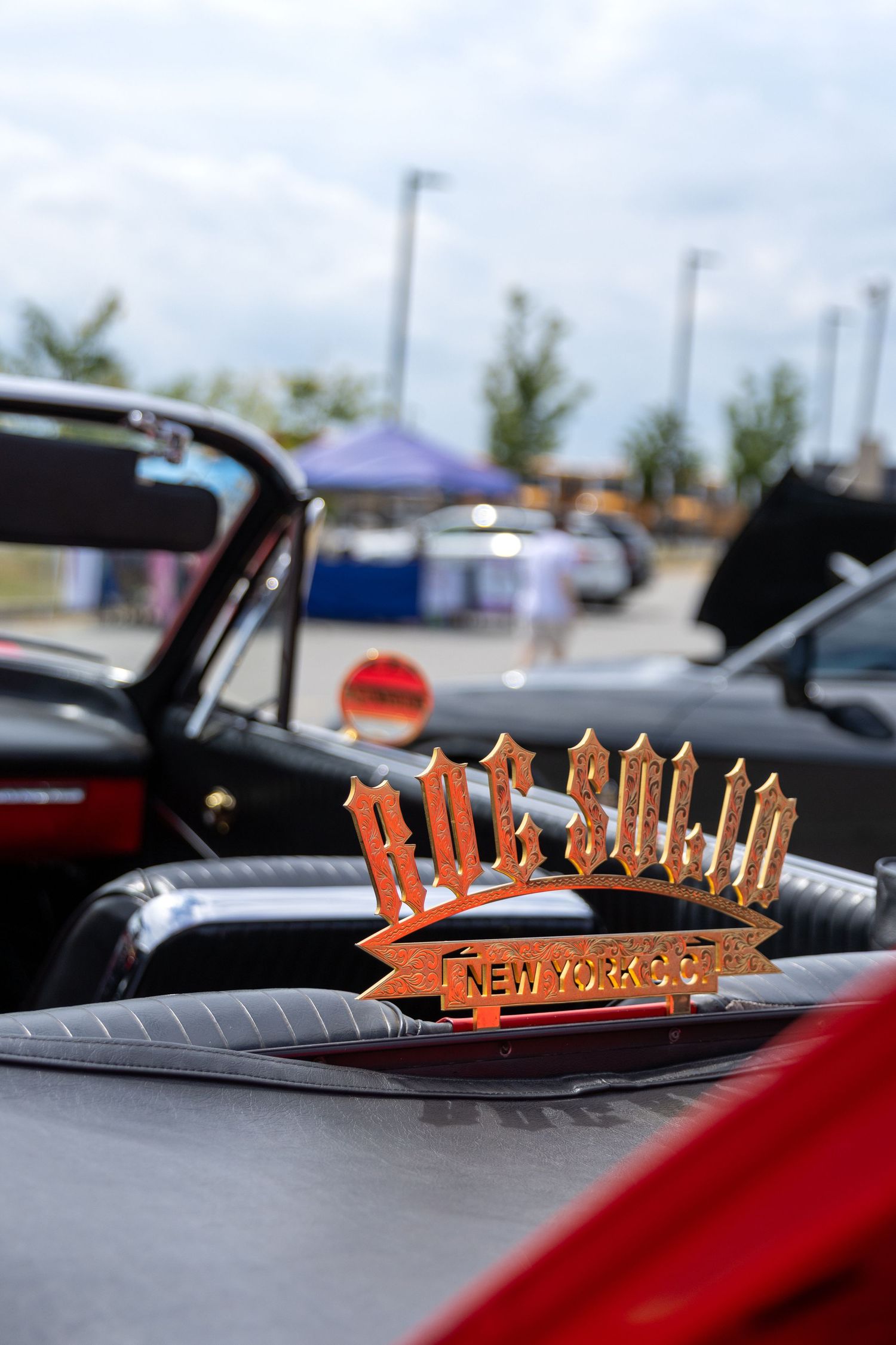 Orange 'Chevrolet' lettering hood ornament on a red classic car at an outdoor car show.