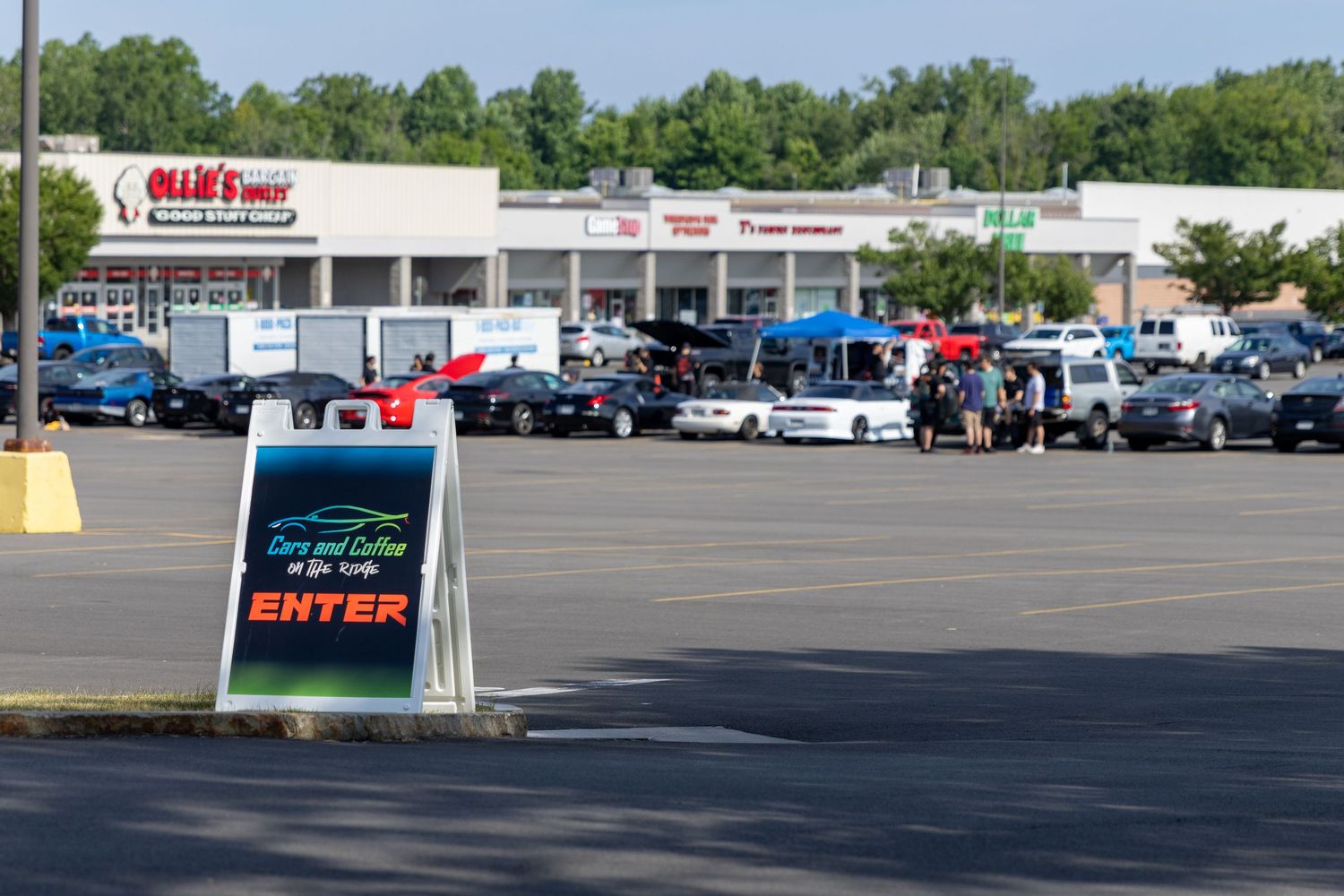 Large commercial parking lot with cars and business signage under sunny blue skies.