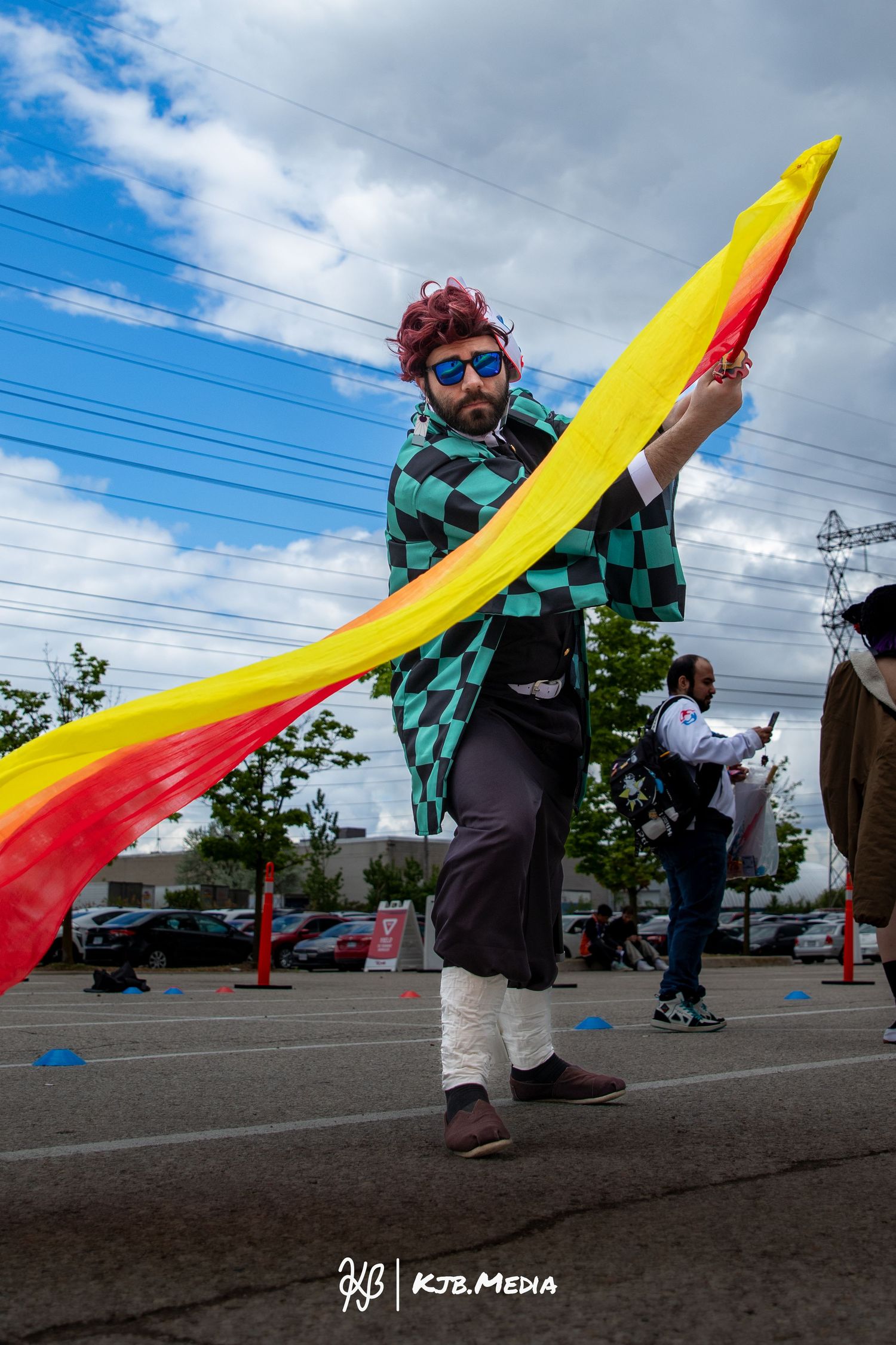 Cosplayer in checkered green outfit performs with a yellow and red prop at an outdoor event.