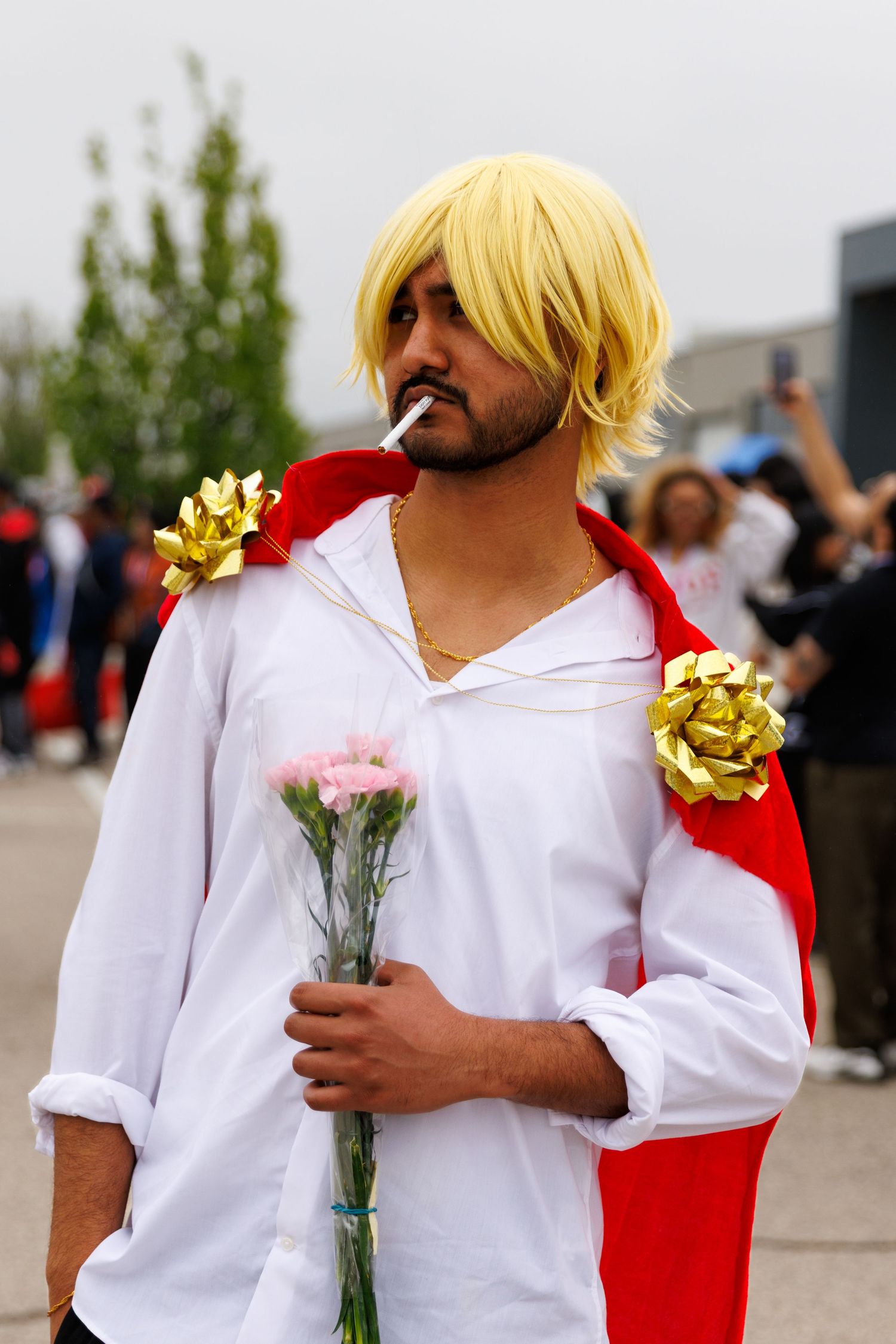 Man cosplaying as Sanji from One Piece in white shirt with blonde wig holding pink flowers.