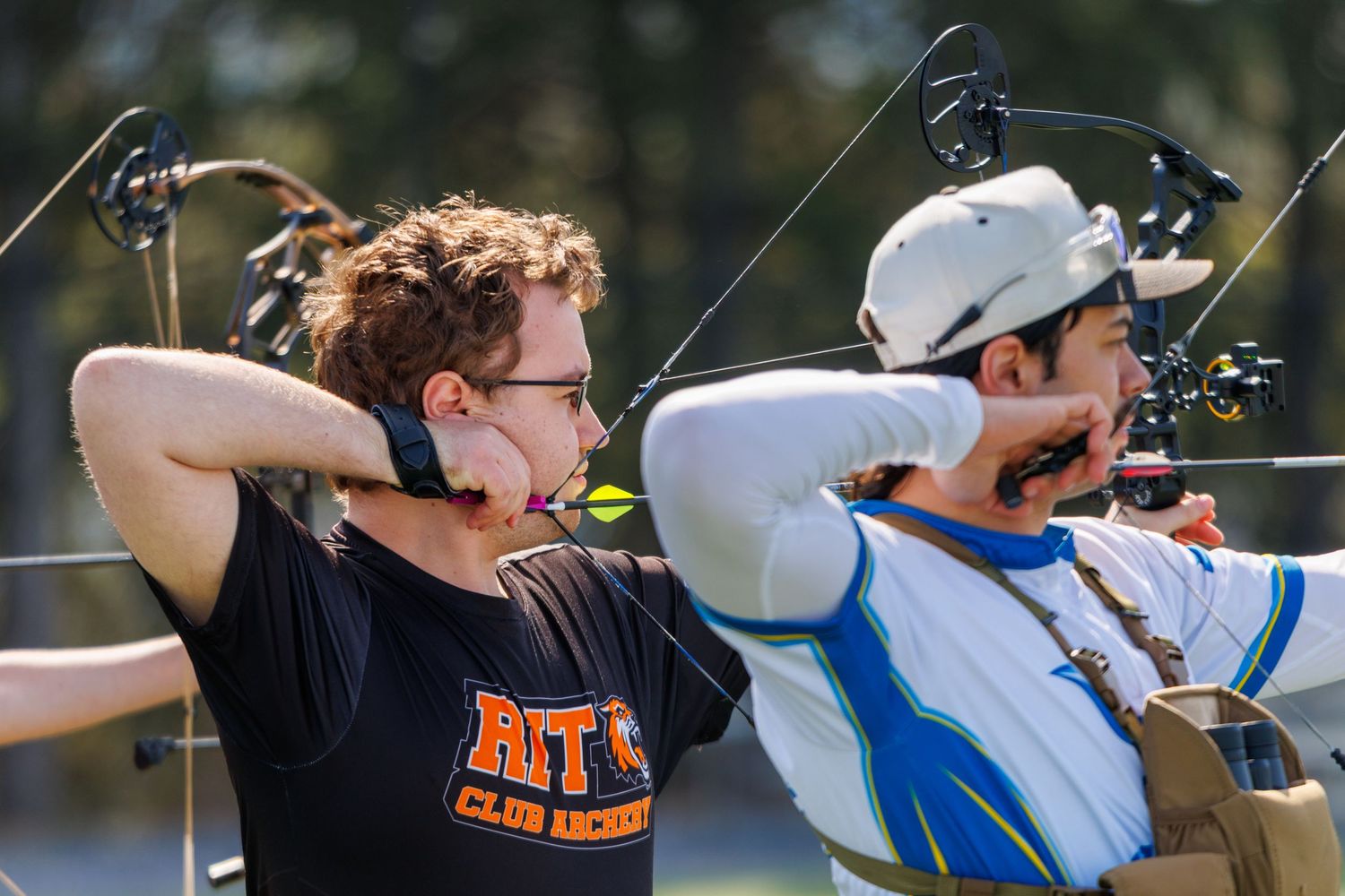 Two male archers drawing their bows simultaneously during an outdoor archery competition.