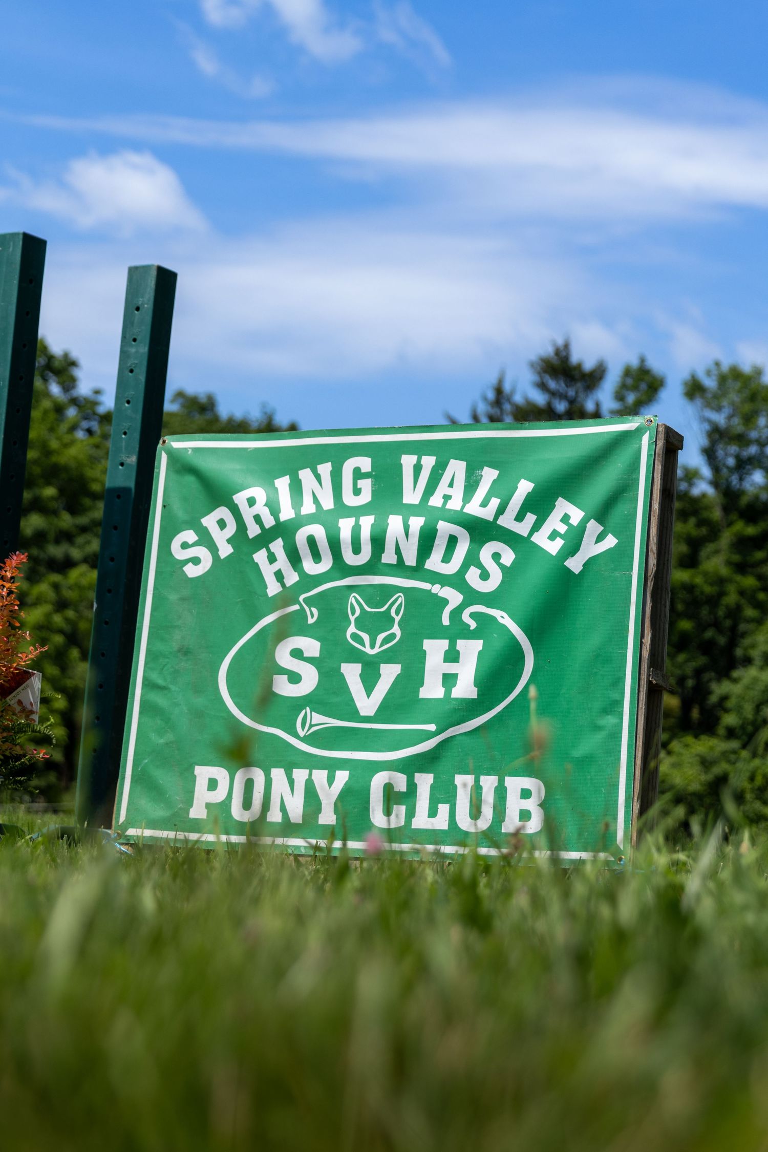 Green sign for Spring Valley Hounds Pony Club mounted between posts in grass.