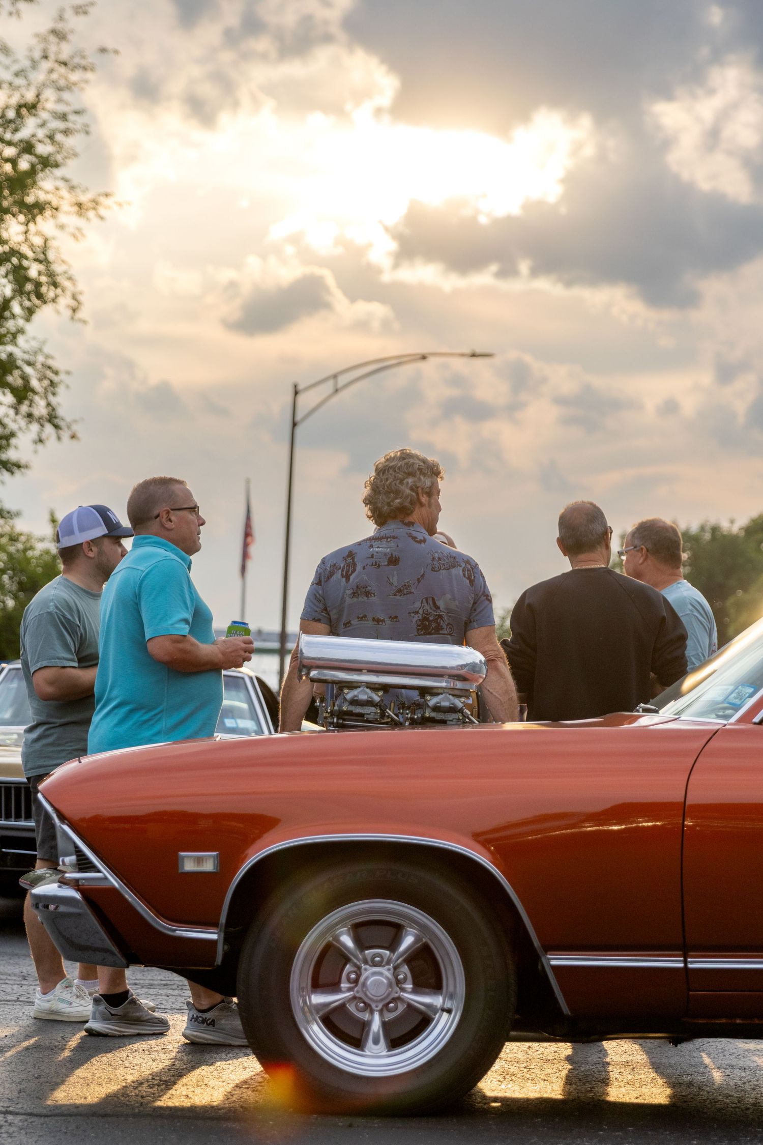 Classic red convertible car shown from multiple angles at sunset with chrome wheels and spectators admiring the vehicle.