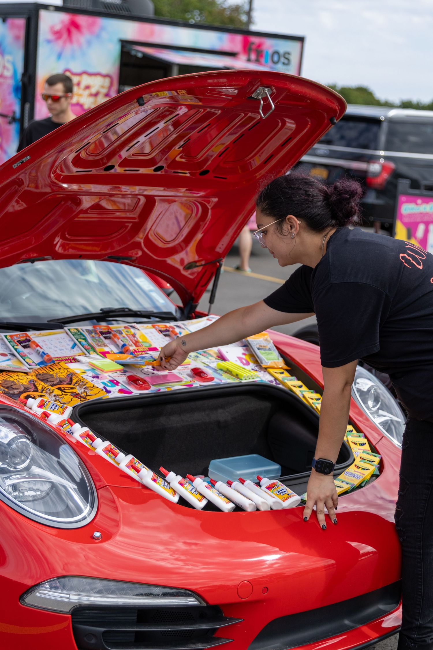 A series of photos showing manga books being arranged on the hood of a bright red sports car.