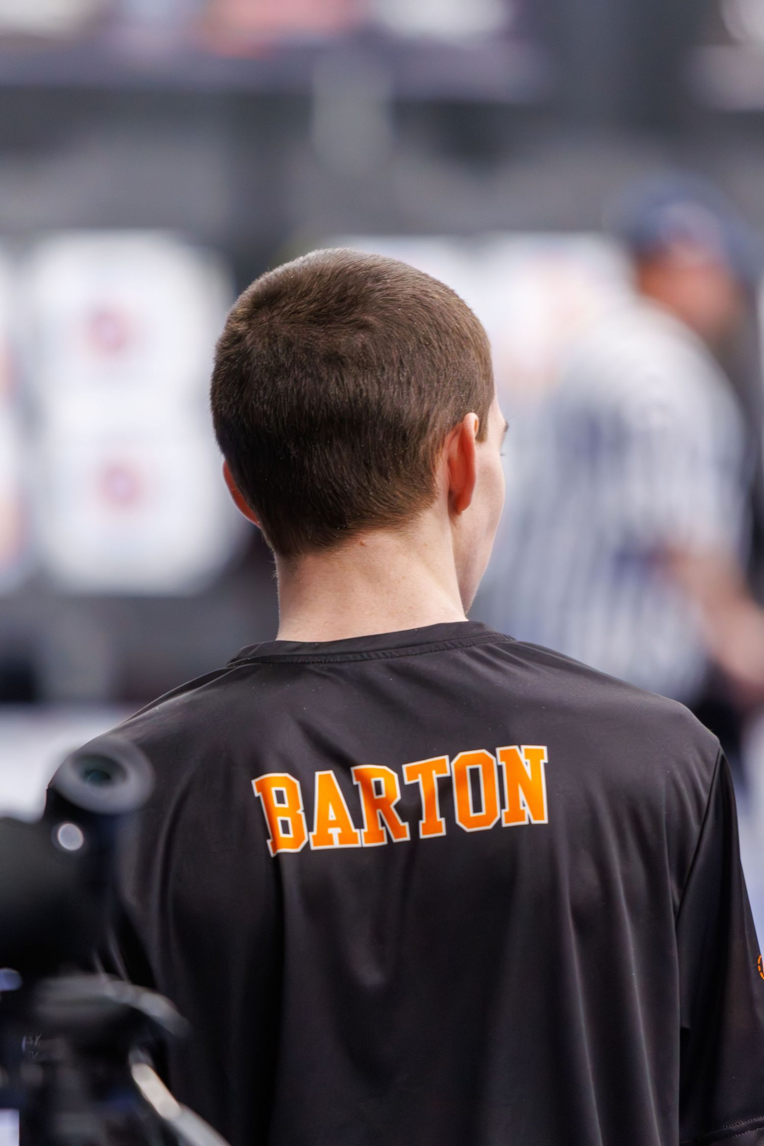 Back view of a man wearing a black Barton jersey at a sporting event.