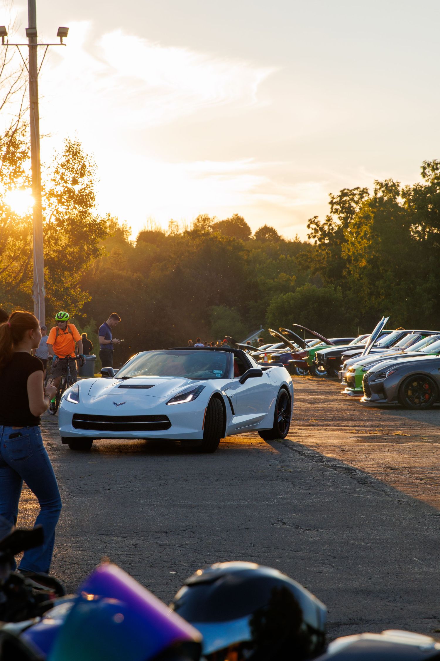 A row of Chevrolet Corvettes parked at a sunset car meet with golden light illuminating the scene.