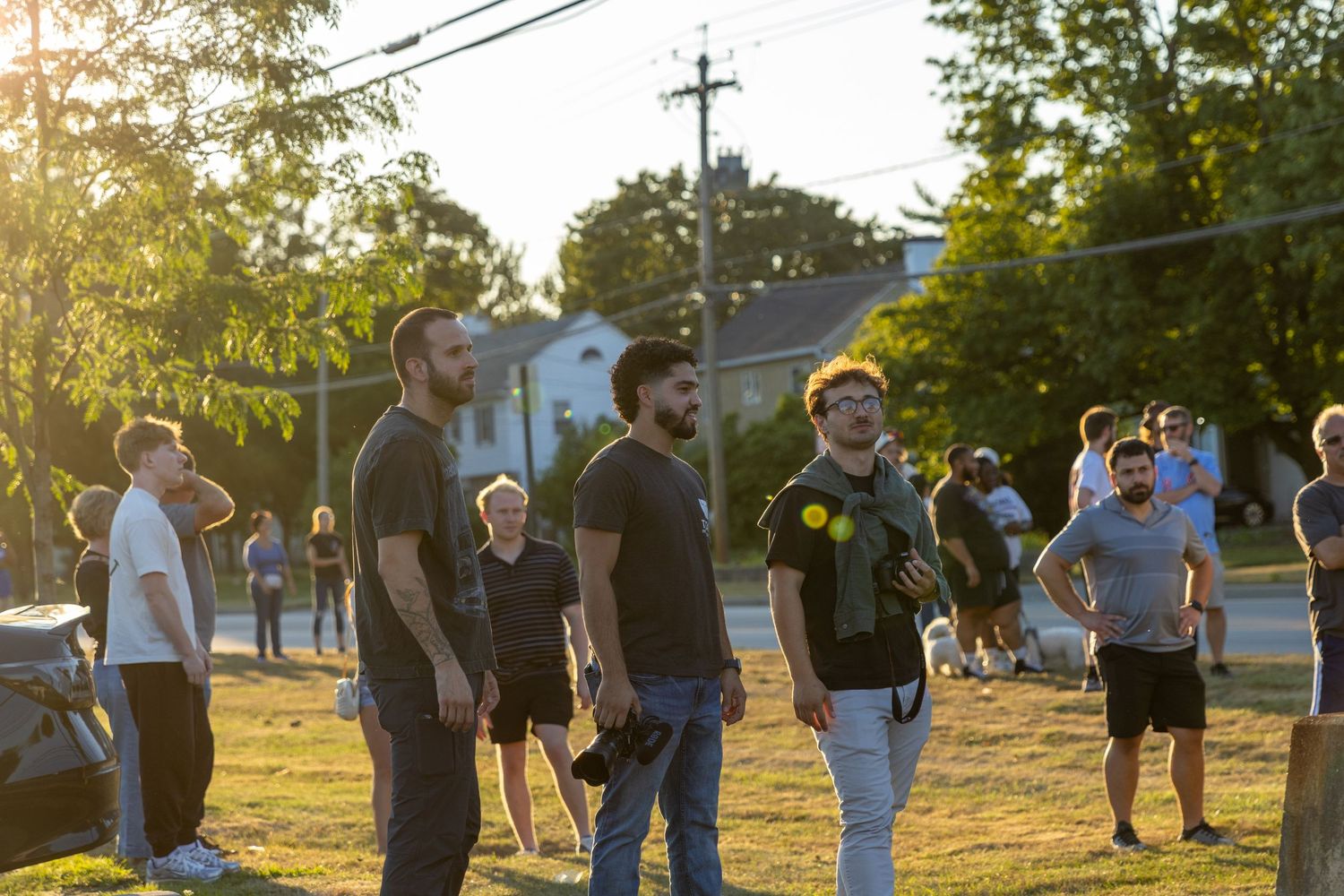 A group gathers for outdoor line dancing in late afternoon sunlight on a grassy area near utility poles.