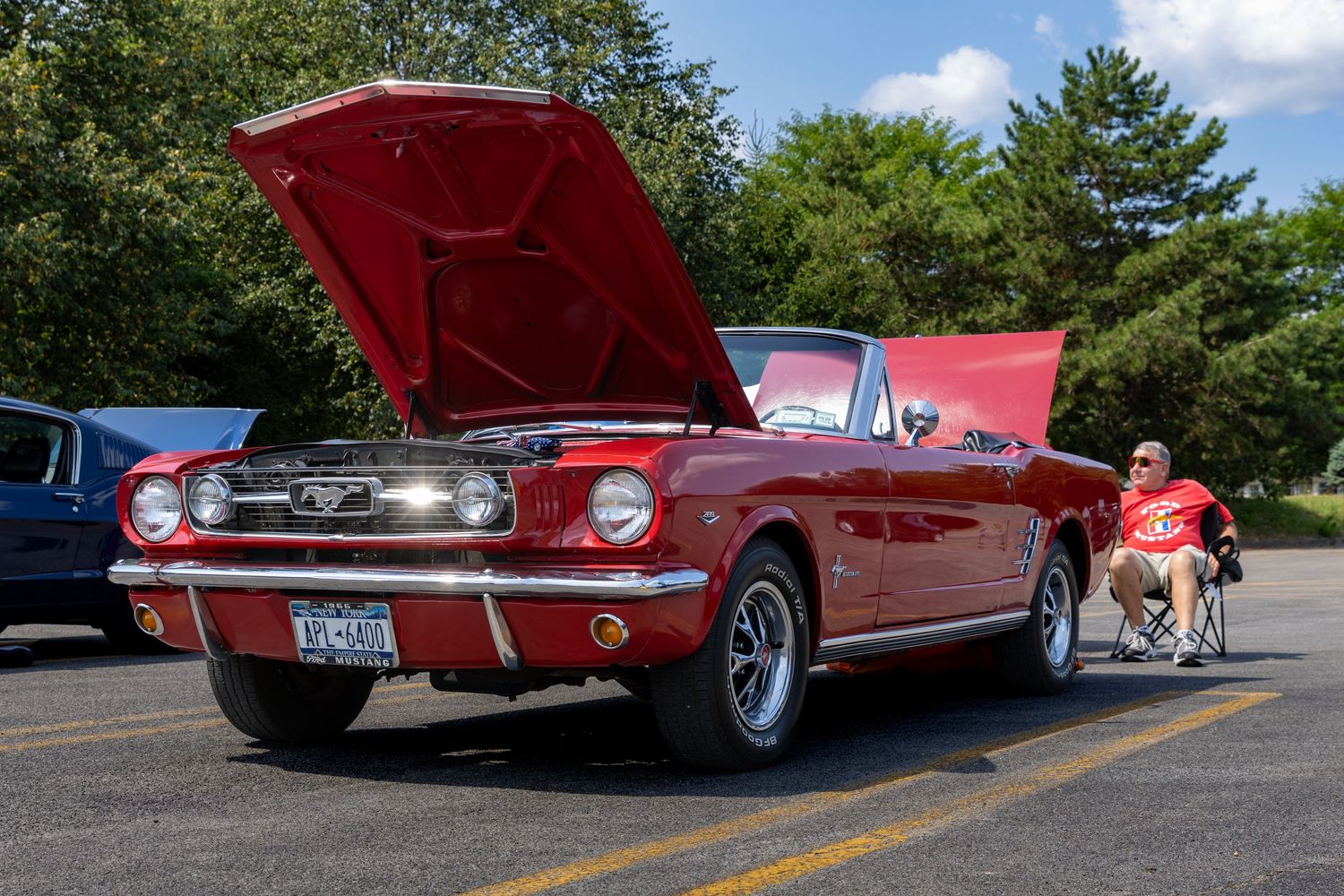 A row of classic red vintage cars displayed at an outdoor car show under sunny skies.