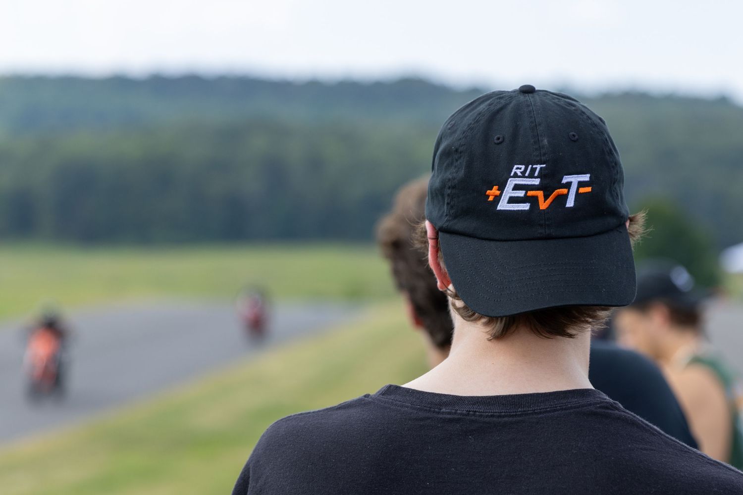 Two racers on motorcycles compete in a motorsport race on a scenic track with green fields in the background.