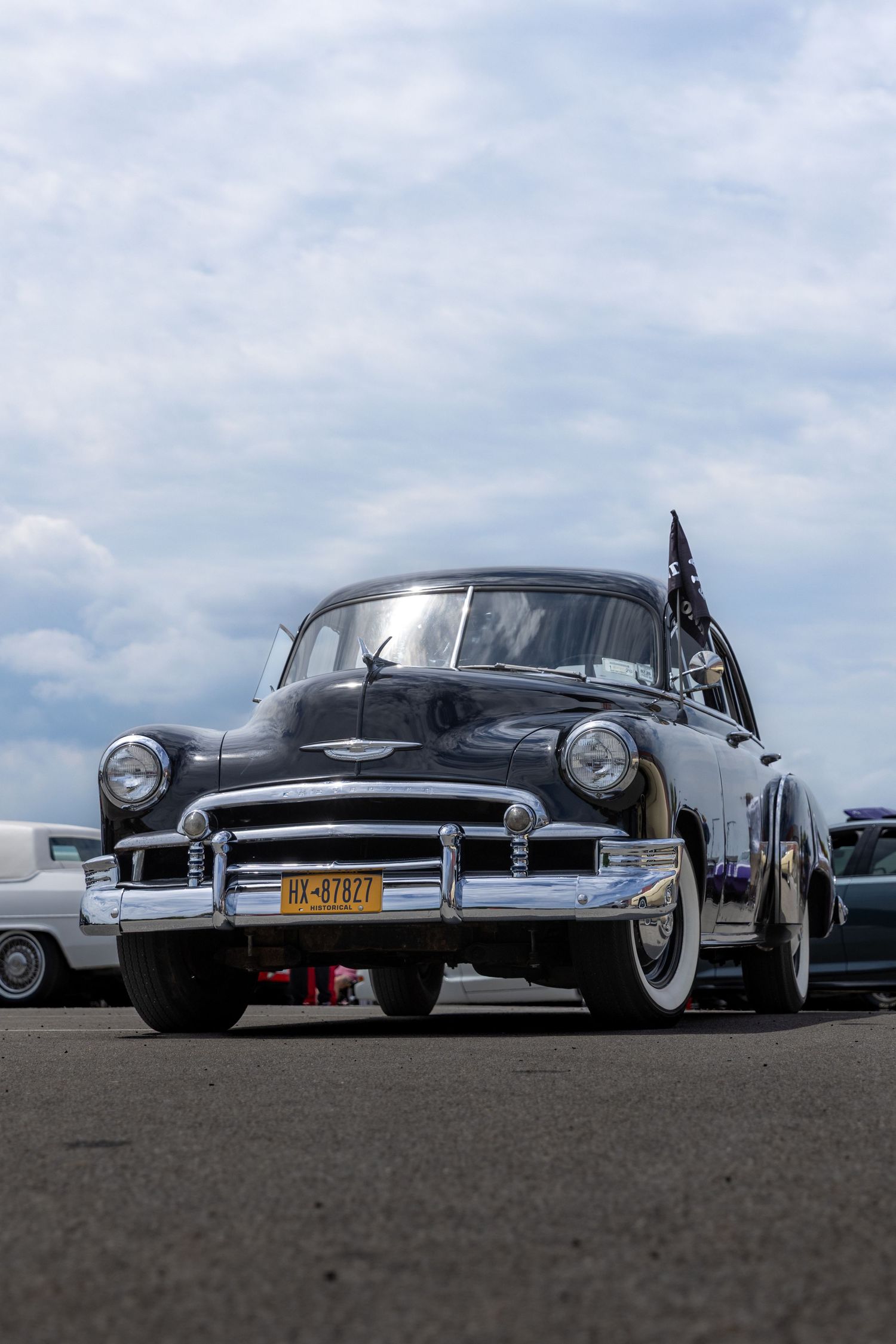 Three classic black vintage cars lined up in a low-angle shot against a cloudy sky, showcasing their sleek chrome details.