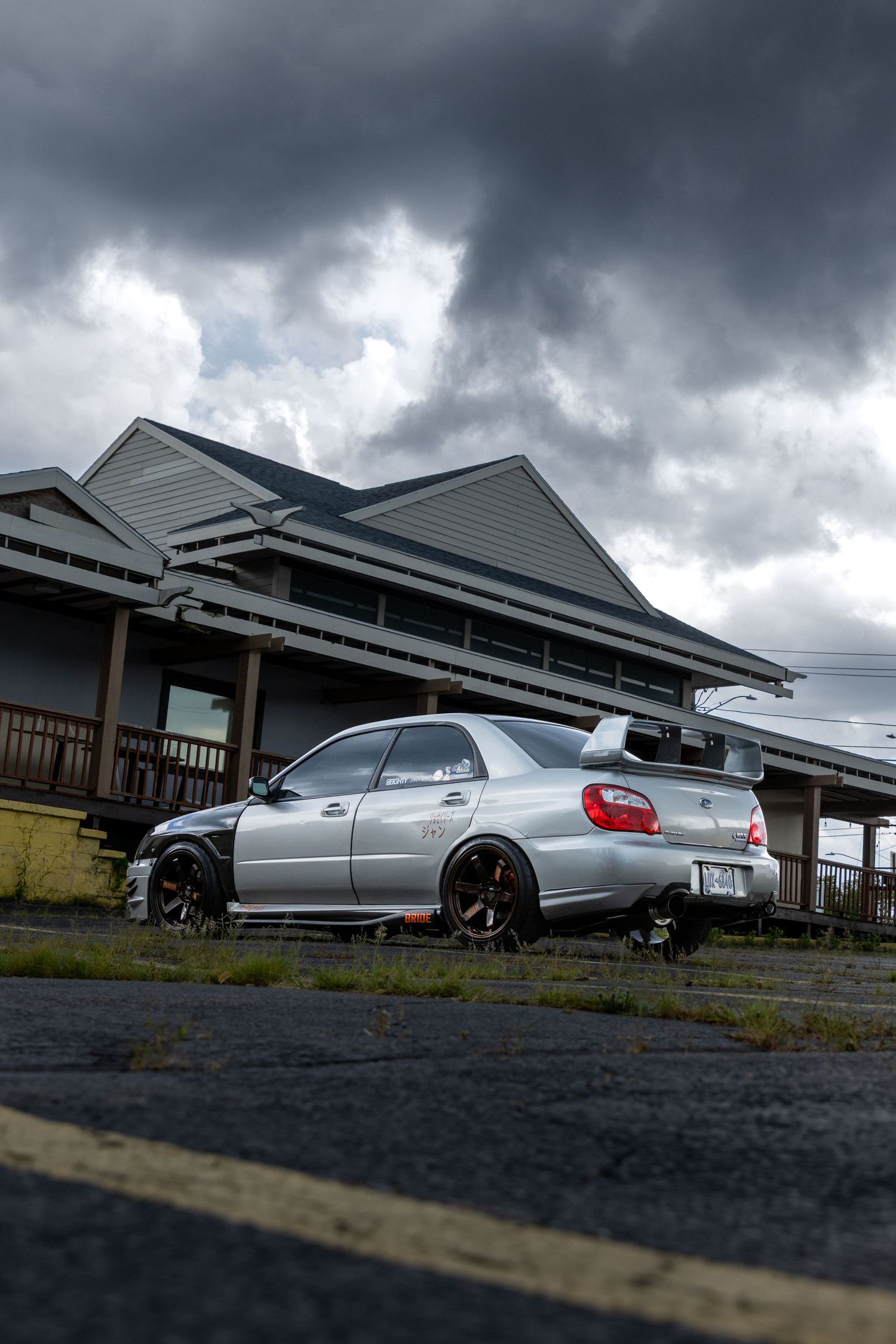 A silver Subaru WRX parked in front of a building under dramatic stormy clouds.