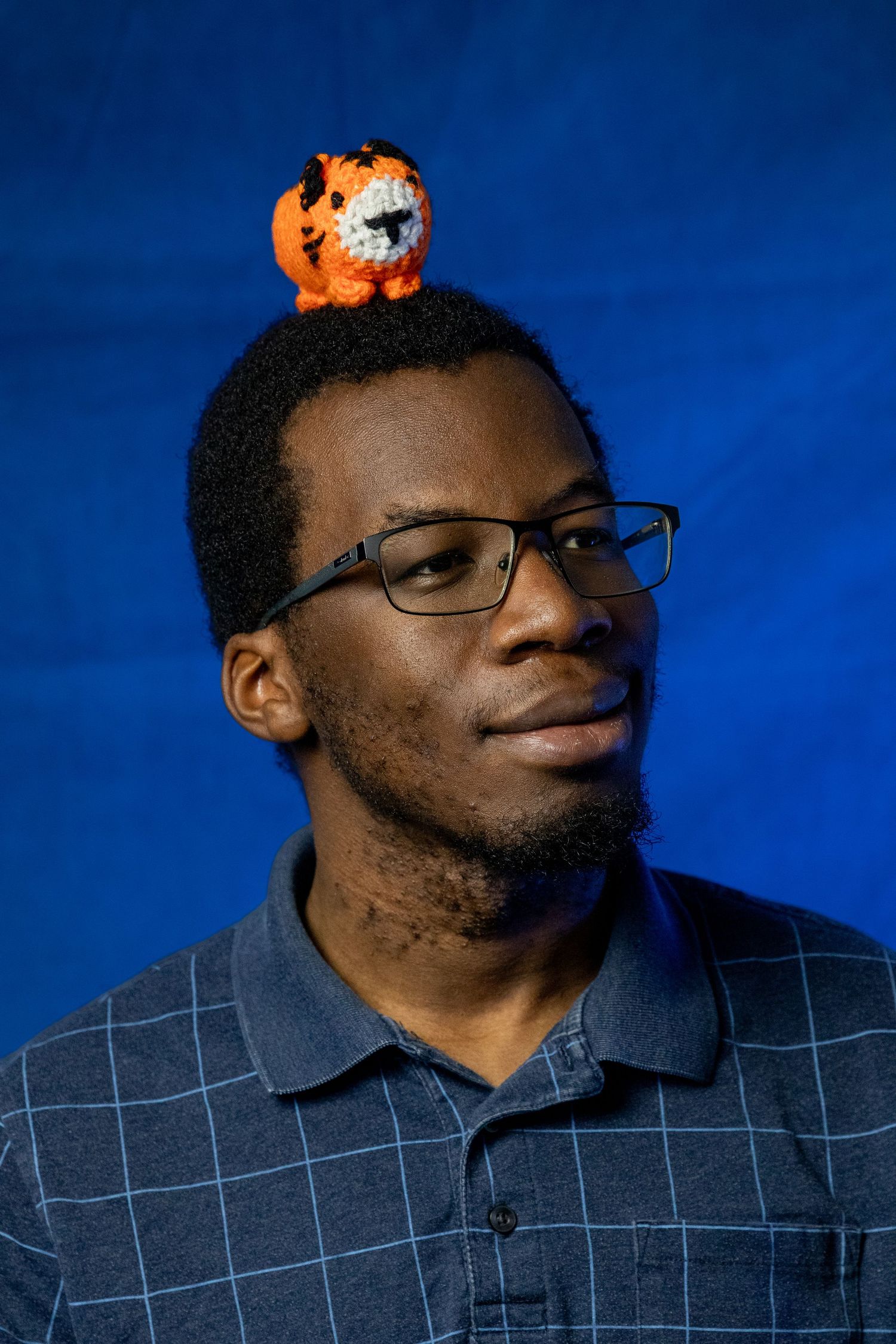 Person in a checkered blue polo shirt with glasses against a dark blue backdrop with a small orange object above.