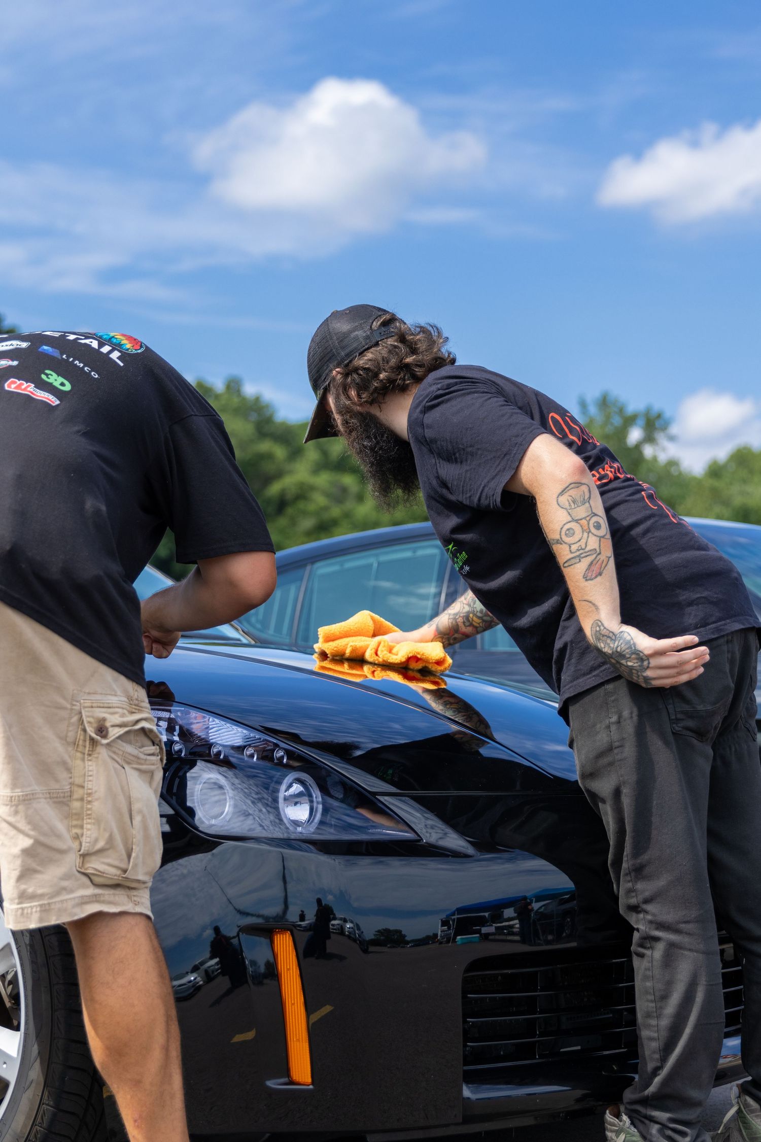 Car detailer in black shirt carefully polishing black luxury vehicle exterior with microfiber cloth on sunny day.