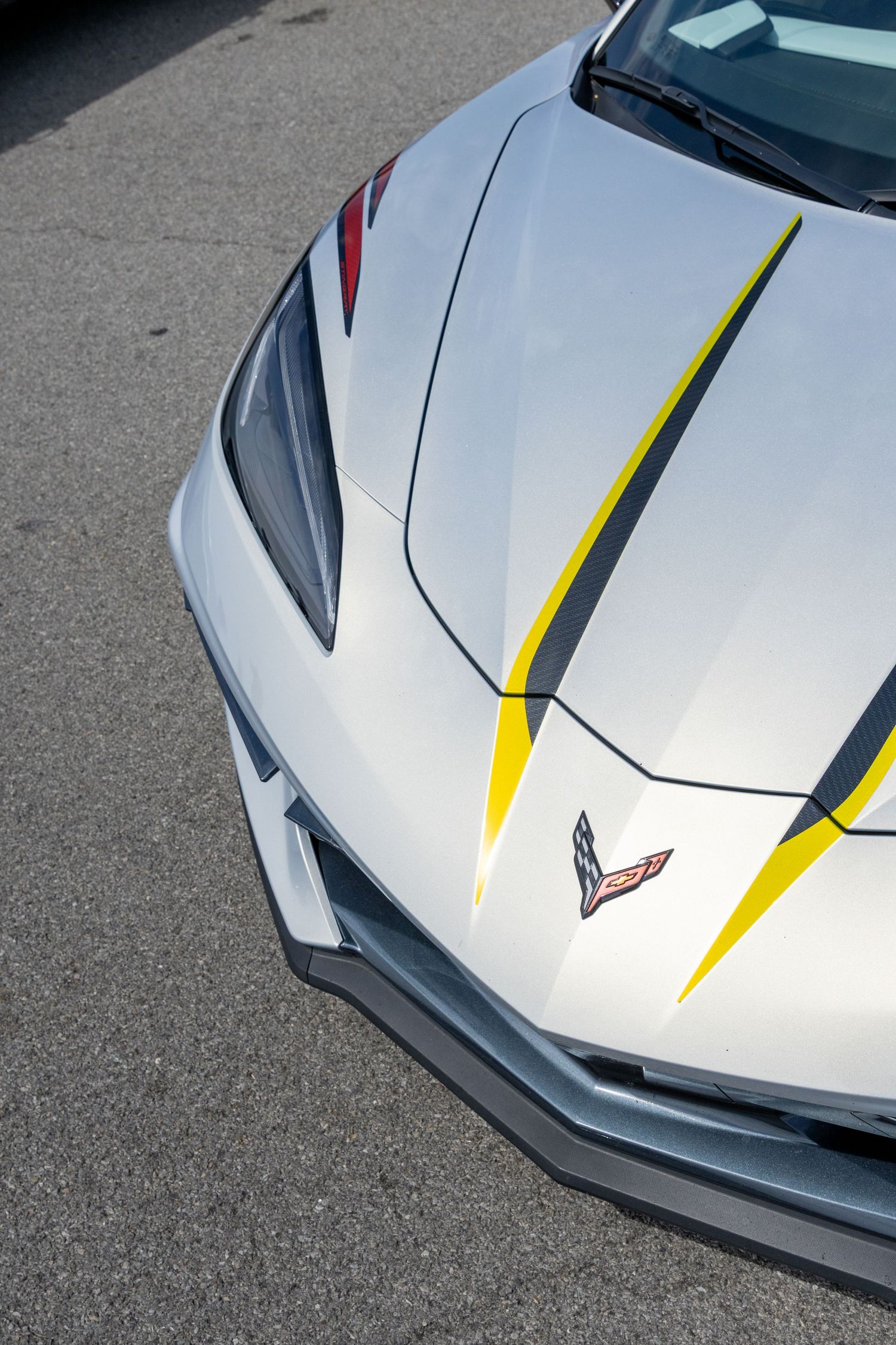 Close-up view of a silver Corvette hood featuring a distinctive yellow and black racing stripe detail.