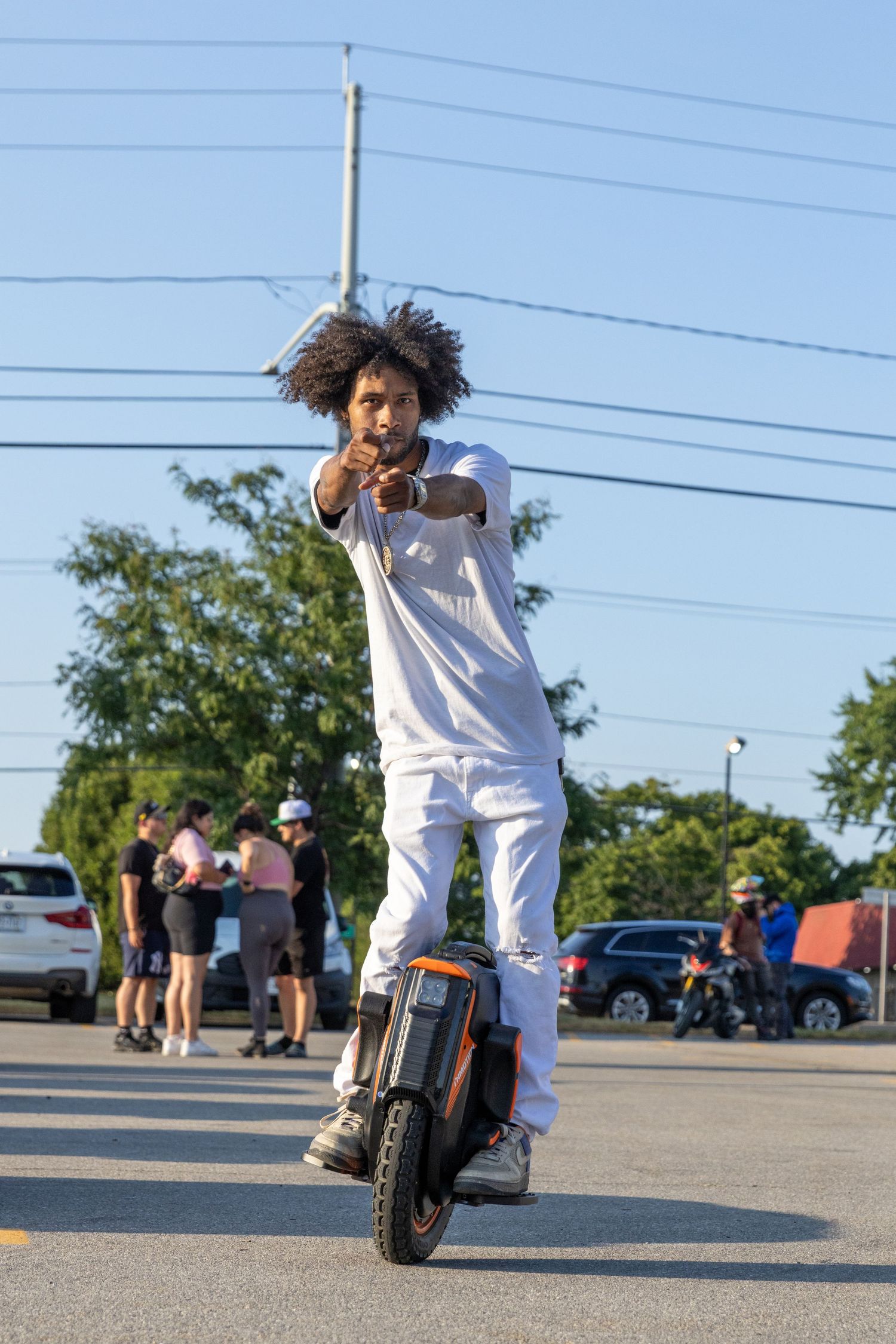 A sequence of three connected photos showing a person in white clothing doing a dance move in a parking lot with a motorcycle nearby.