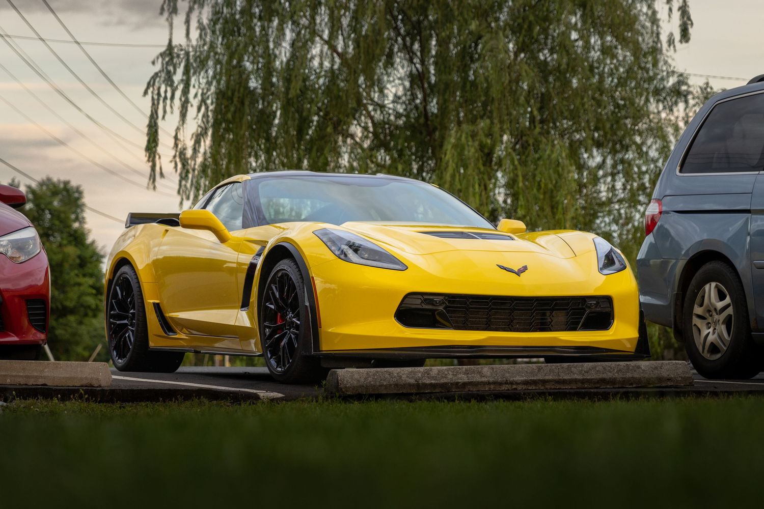 Five bright yellow Chevrolet Corvette sports cars parked in a row showcasing their sleek profiles against a cloudy sky.