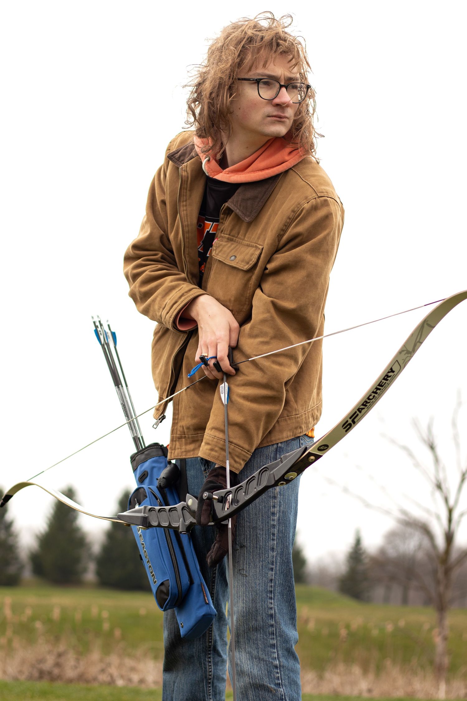 Person in brown jacket practicing archery with bow and arrows outdoors.