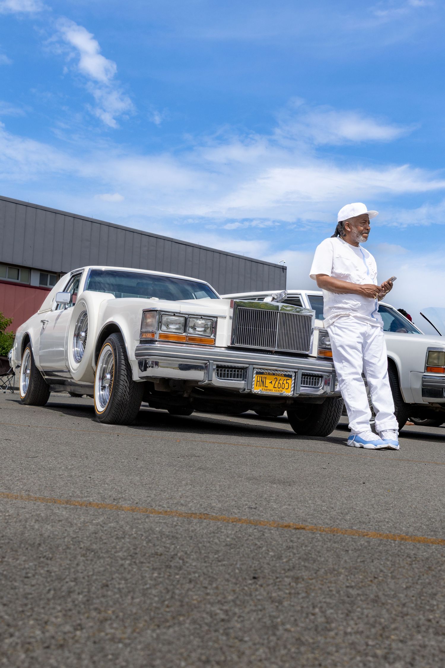 Row of vintage luxury cars lined up at an outdoor car show with buildings in the background.