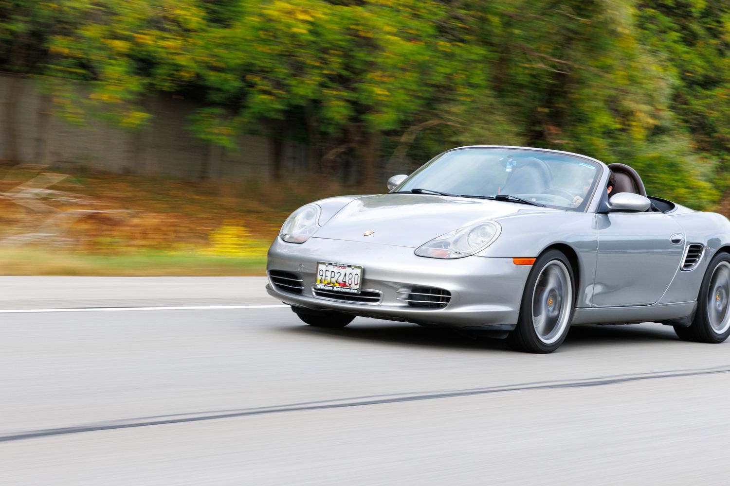 A silver Porsche sports car drives along a winding mountain road with blurred motion effect.