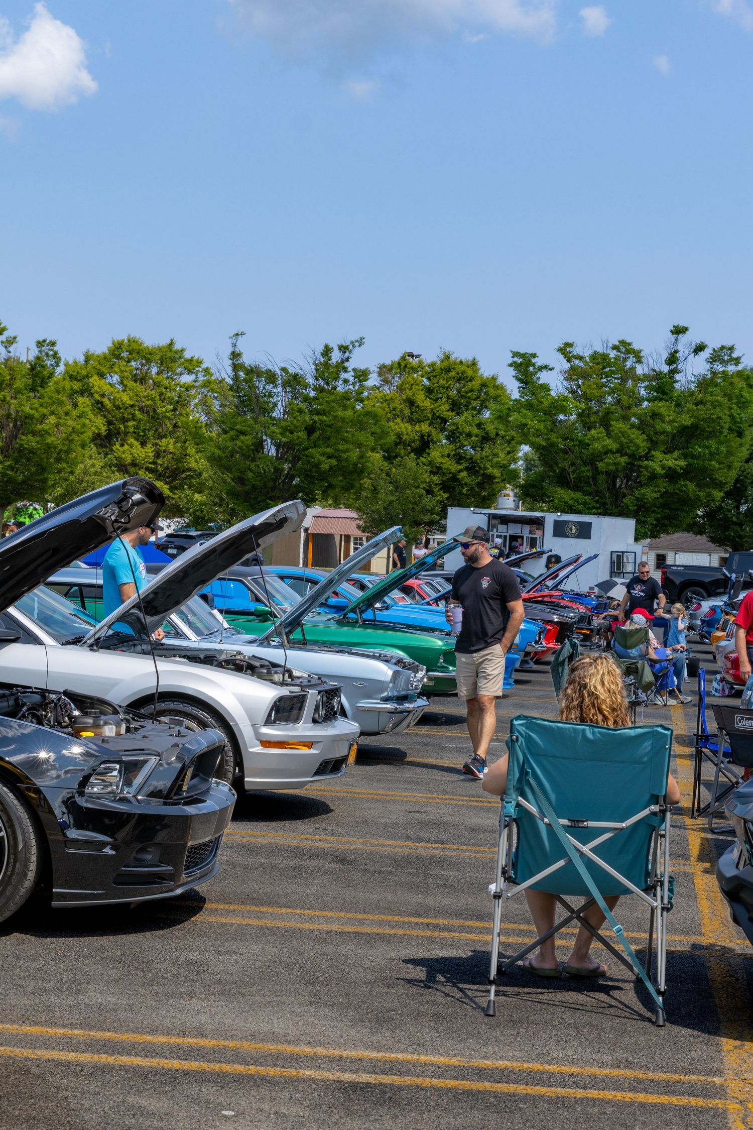 Classic cars on display at an outdoor auto show with folding chairs set up in the parking lot.