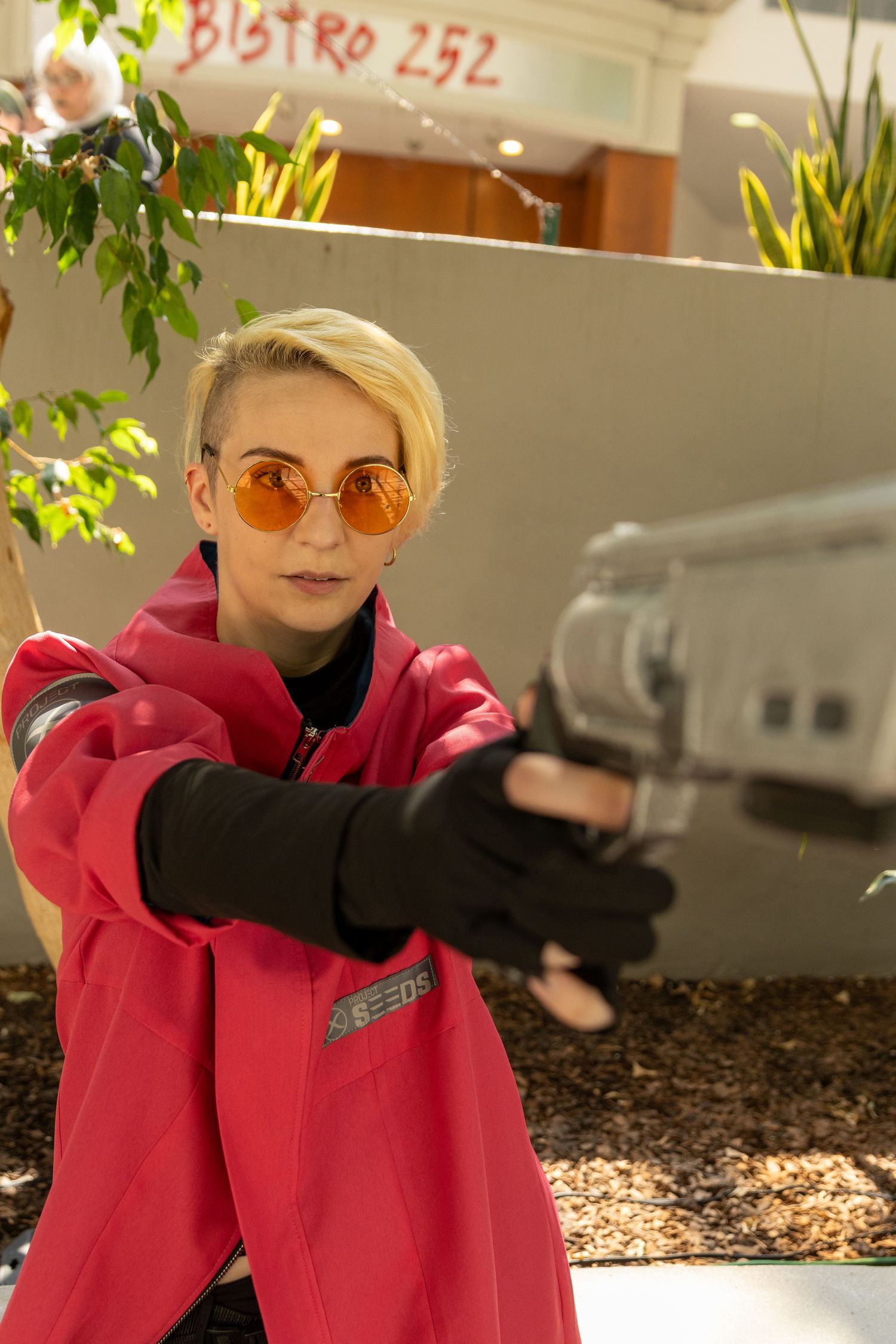 A person in a bright red coat and sunglasses poses playfully in front of a bistro restaurant entrance.