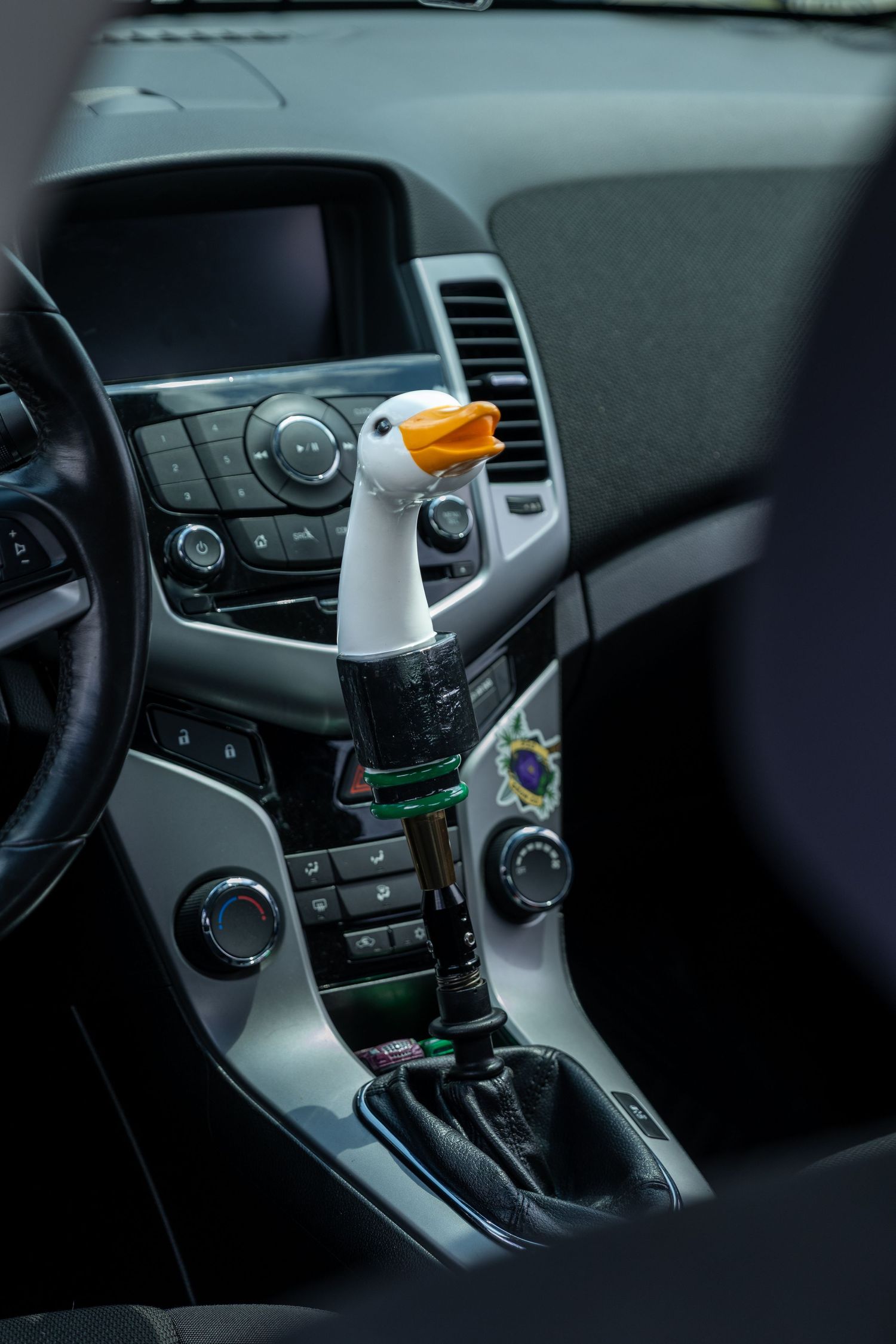 Interior view of a modern car dashboard showing center console controls and an orange rubber duck decoration.