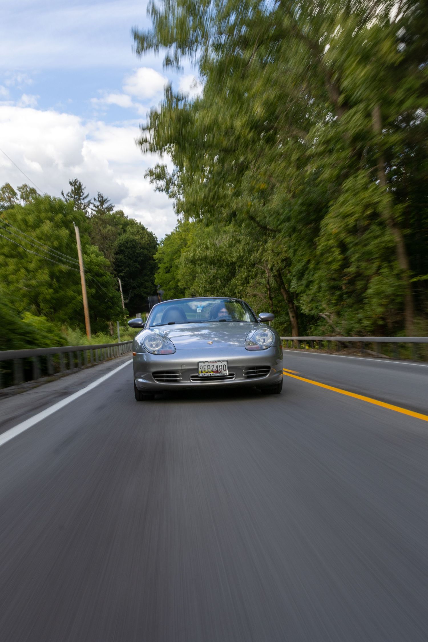 Driving point-of-view sequence on tree-lined road with silver Porsche sports car appearing in gradual frames ahead.