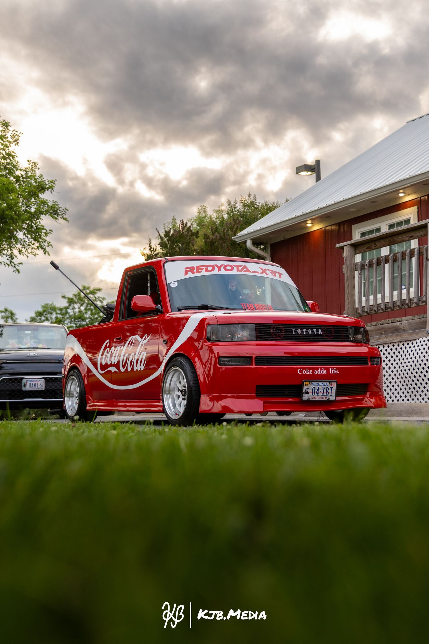 Bright red Coca-Cola themed custom truck displayed in front of a building at dusk.
